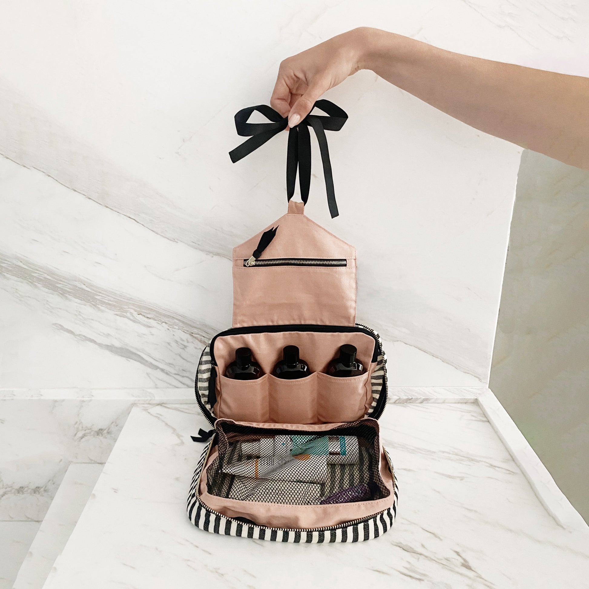 Bag-all Folding/Hanging Toiletry Case in striped cotton featuring three compartments, mesh pocket, and hanging ribbon. Organized storage for toiletries, makeup, and accessories in pink and black design.