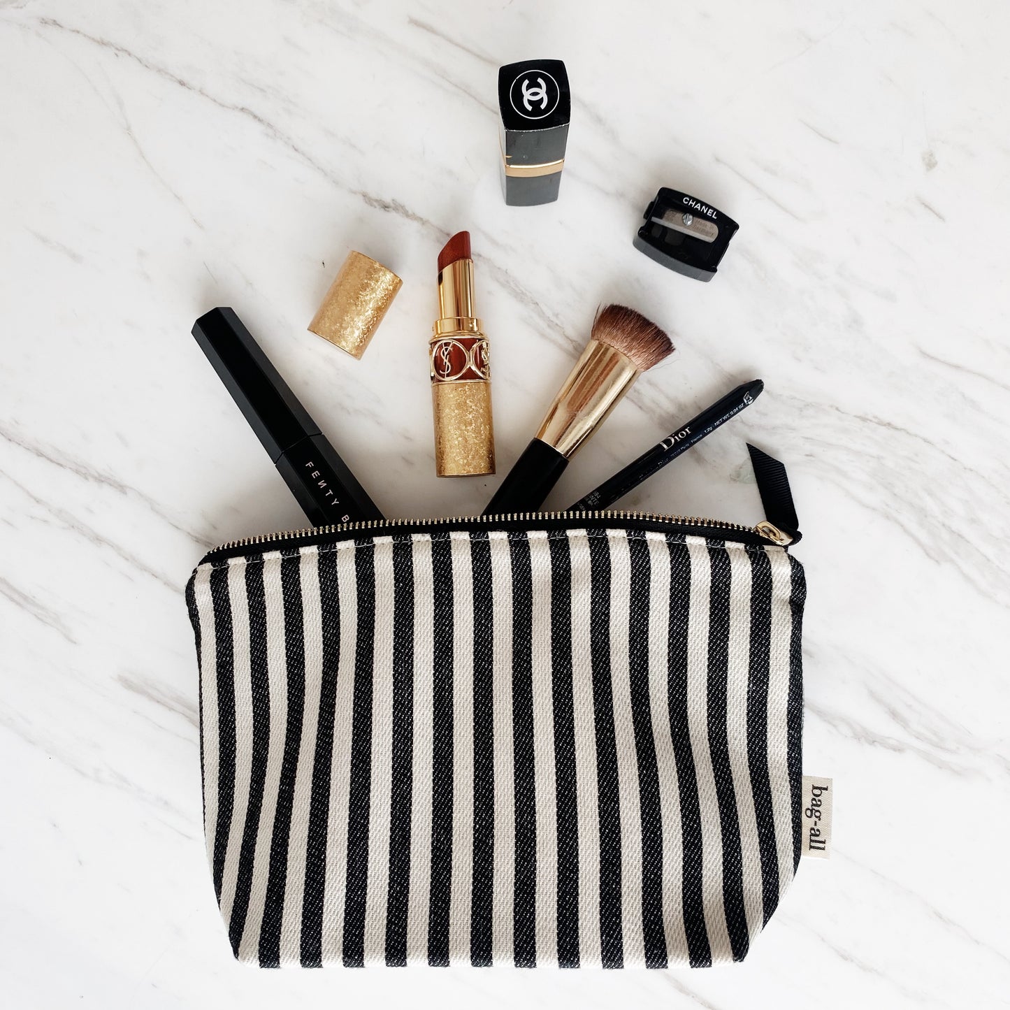 Bag-all Striped Makeup Pouch with black and white stripes, gold zipper, and pink lining, shown with luxury makeup essentials on marble surface, perfect for organizing cosmetics and beauty tools