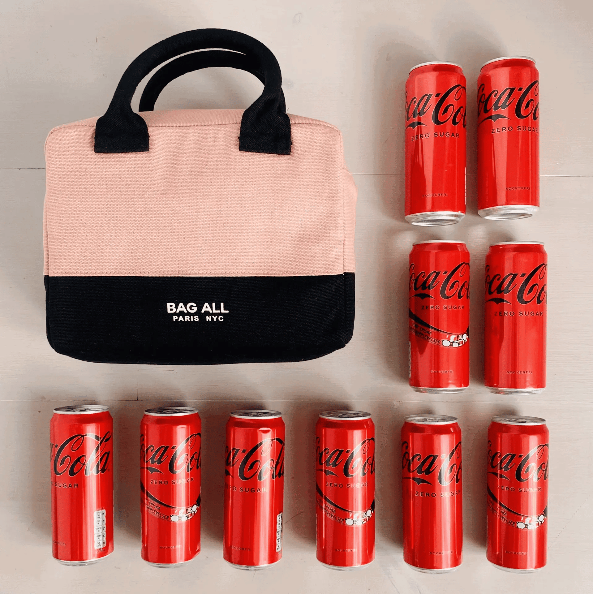Bag-all Stylish Monogram Lunch Box in pink and black insulated design, displayed with Coca-Cola cans showing size comparison. Features soft handles and brand logo, perfect for daily meals.