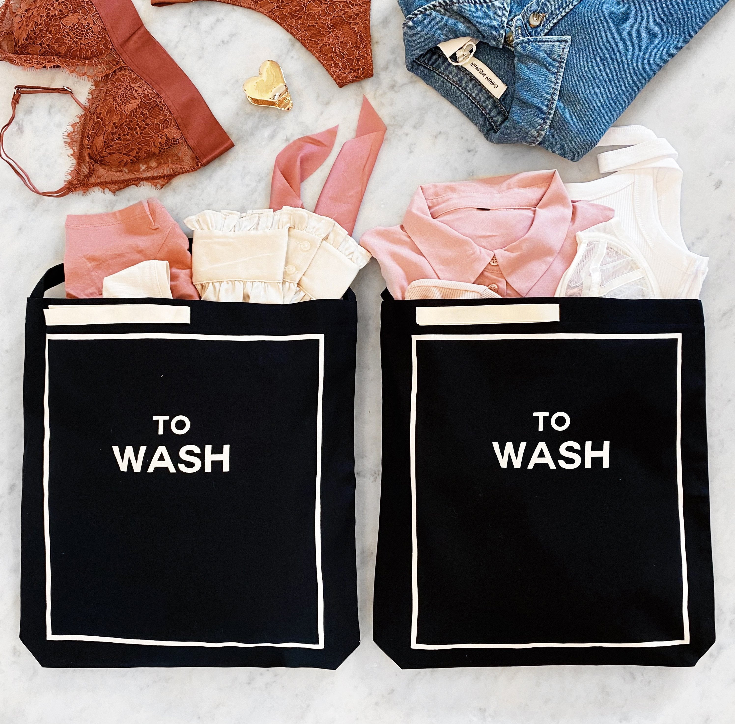 Bag-all To Wash Laundry Bag in black cotton with white border detail, filled with pink and neutral clothing items, displayed on marble surface, perfect for organizing dirty laundry