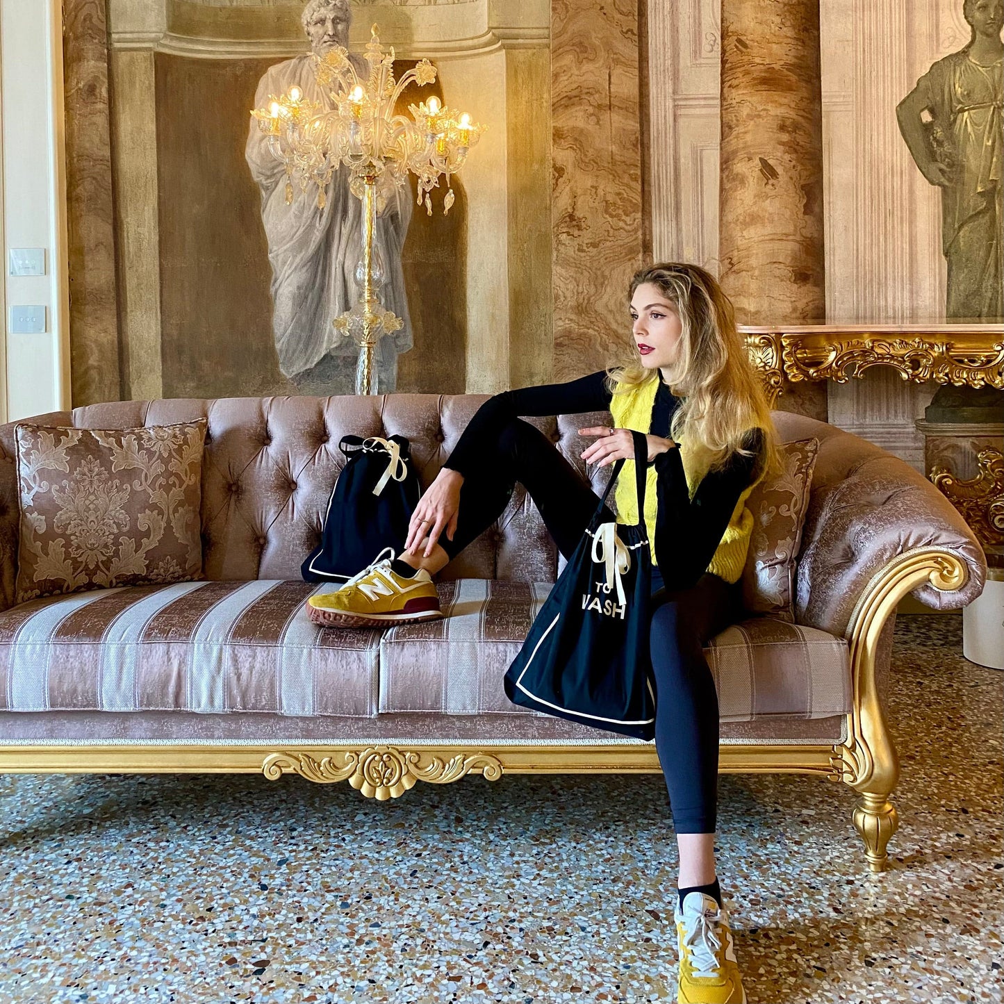 Bag-all To Wash Laundry Bag in black shown in luxurious setting with vintage sofa, crystal chandelier and elegant interior, highlighting practical travel organization and style