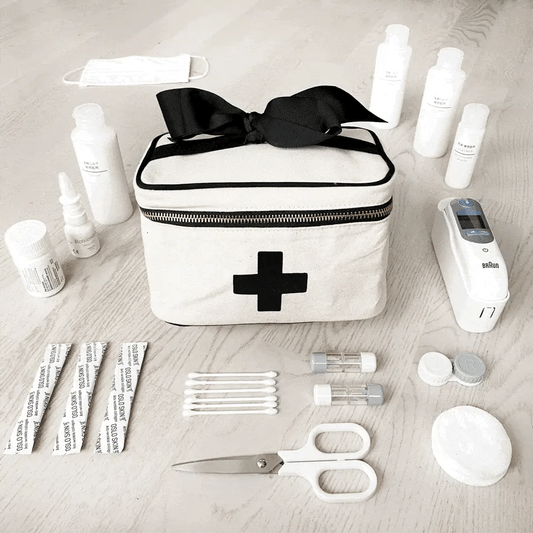 Bag-all Meds and First Aid Storage Box in cream with black cross design, black bow accent, and zipper closure, surrounded by medical supplies