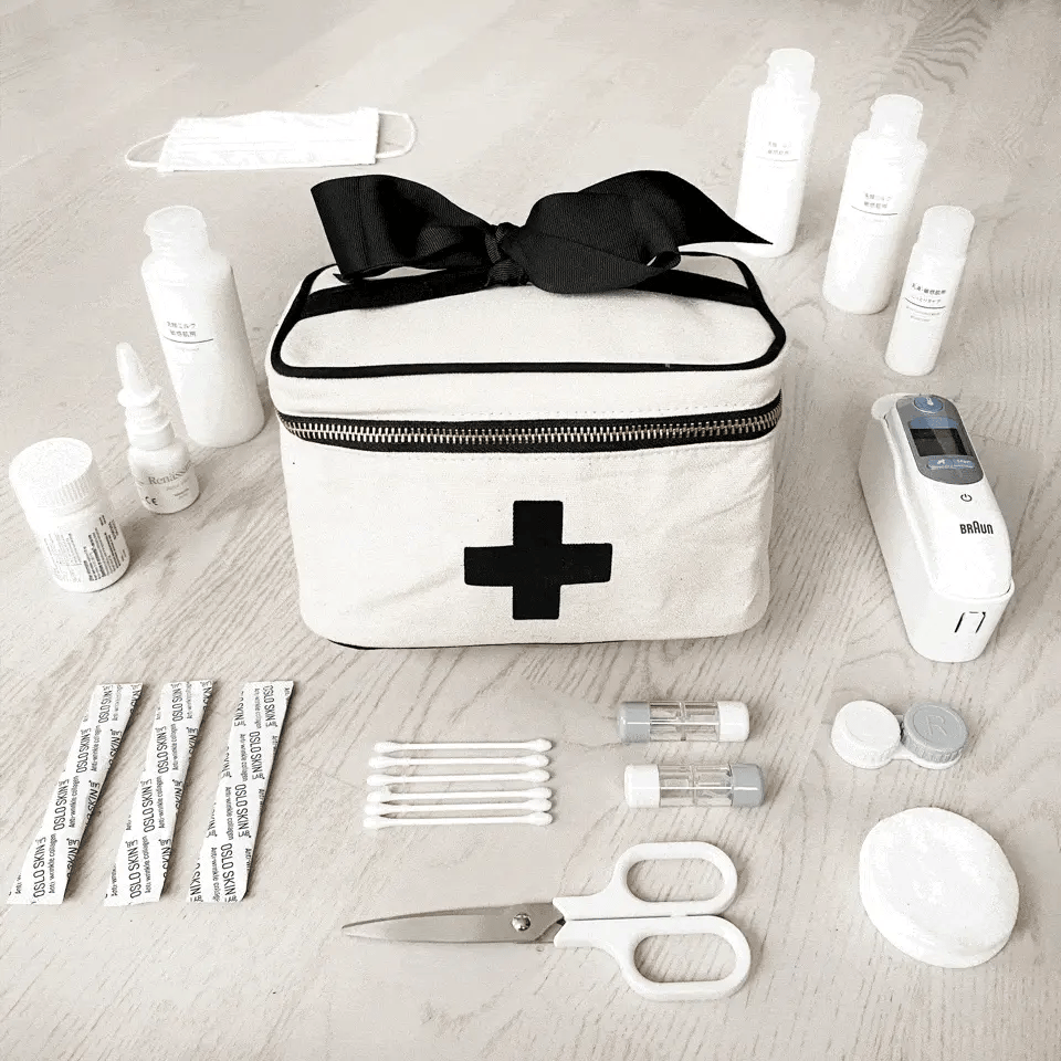Bag-all Meds and First Aid Storage Box in cream with black cross design, black bow accent, and zipper closure, surrounded by medical supplies