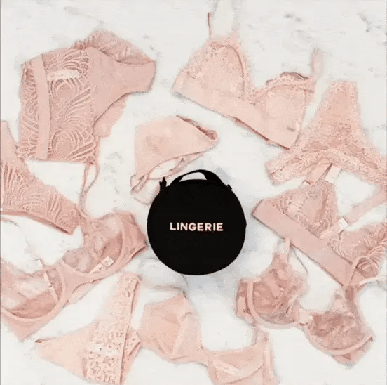 Bag-all Round Lingerie Case in Black surrounded by blush pink lace lingerie pieces arranged in a circular pattern on white marble surface, showcasing elegant storage solution