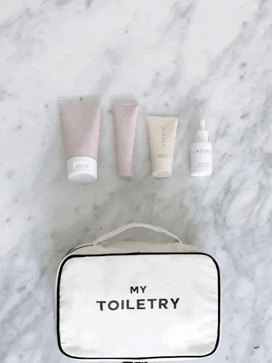 Bag-all Folding/Hanging Toiletry Case in cream with 'My Toiletry' text, displayed with pink and neutral skincare products on marble surface, showcasing organized travel storage