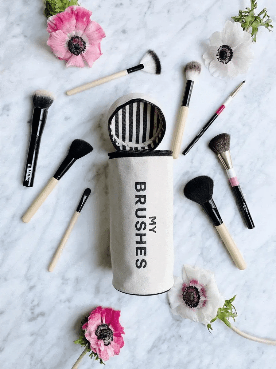 Bag-all My Brushes makeup brush organizer with elegant anemone flowers on marble background, featuring professional cosmetic brushes arranged artistically around striped case