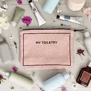 Bag-all Pink Toiletry Pouch with waterproof lining surrounded by beauty essentials and flowers on grey surface, featuring black zipper and text "My Toiletry