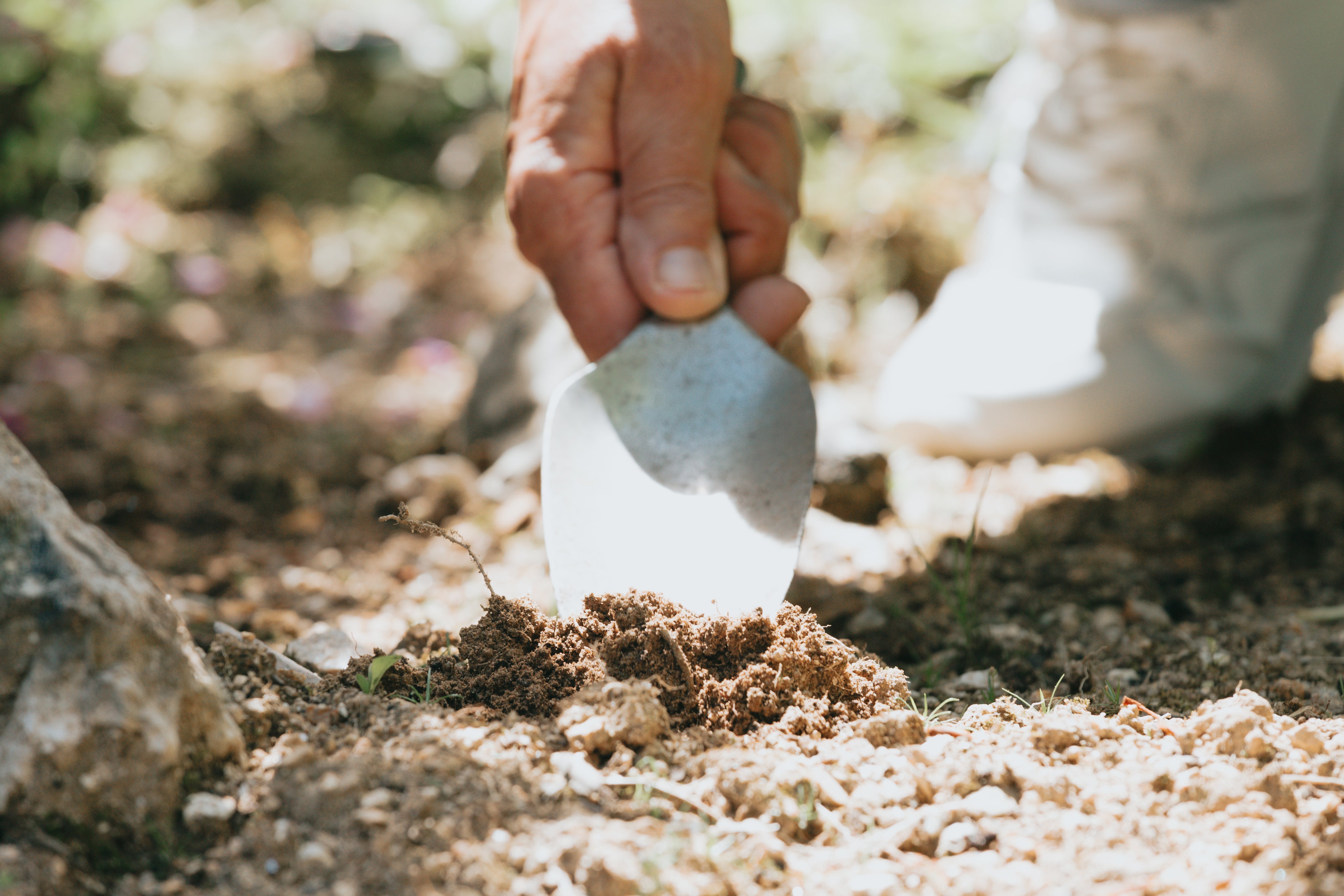 Close-up of hand digging soil with a gardening trowel, symbolizing care and attention in everyday tasks for Bag-all’s travel and organization spirit