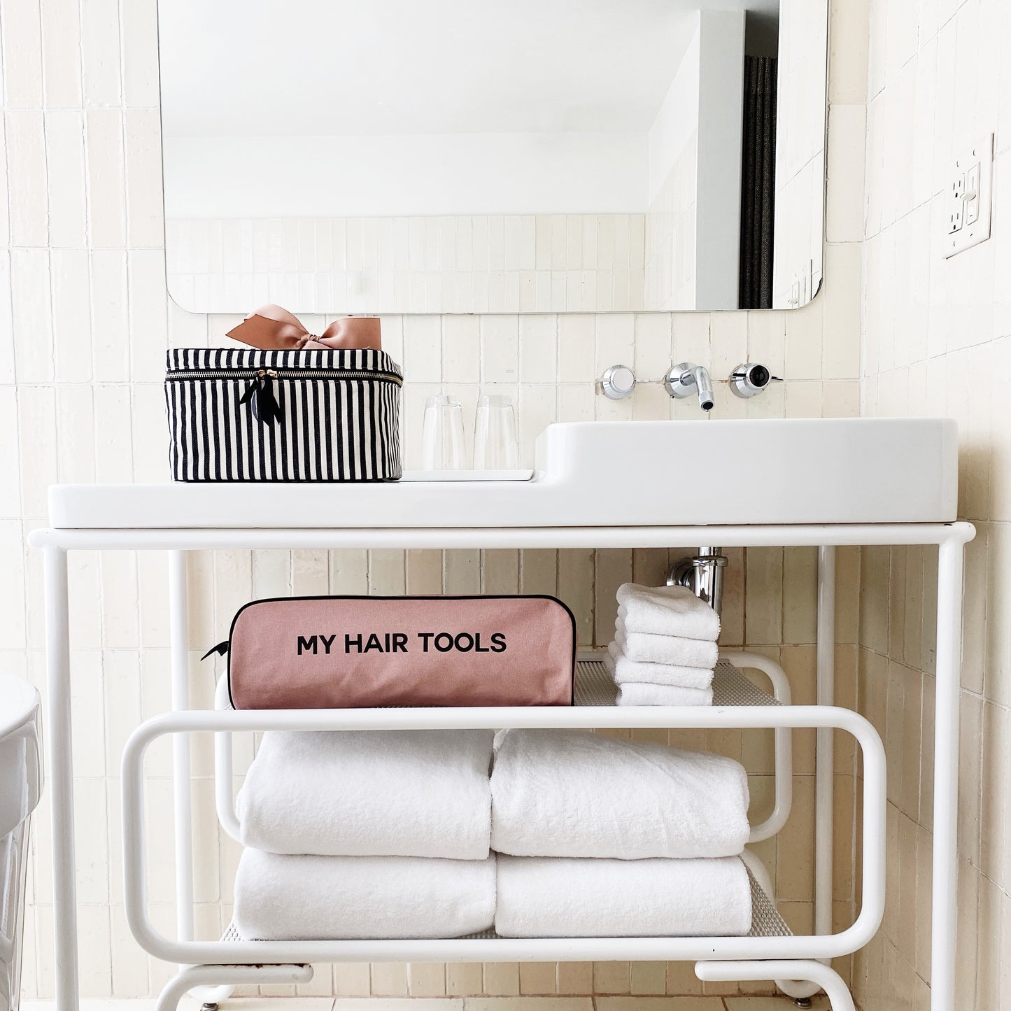 Bag-all Roomy Hair Wrap Tools Travel Case in pink blush displayed on white bathroom shelf with towels, showcasing stylish storage for hair styling tools