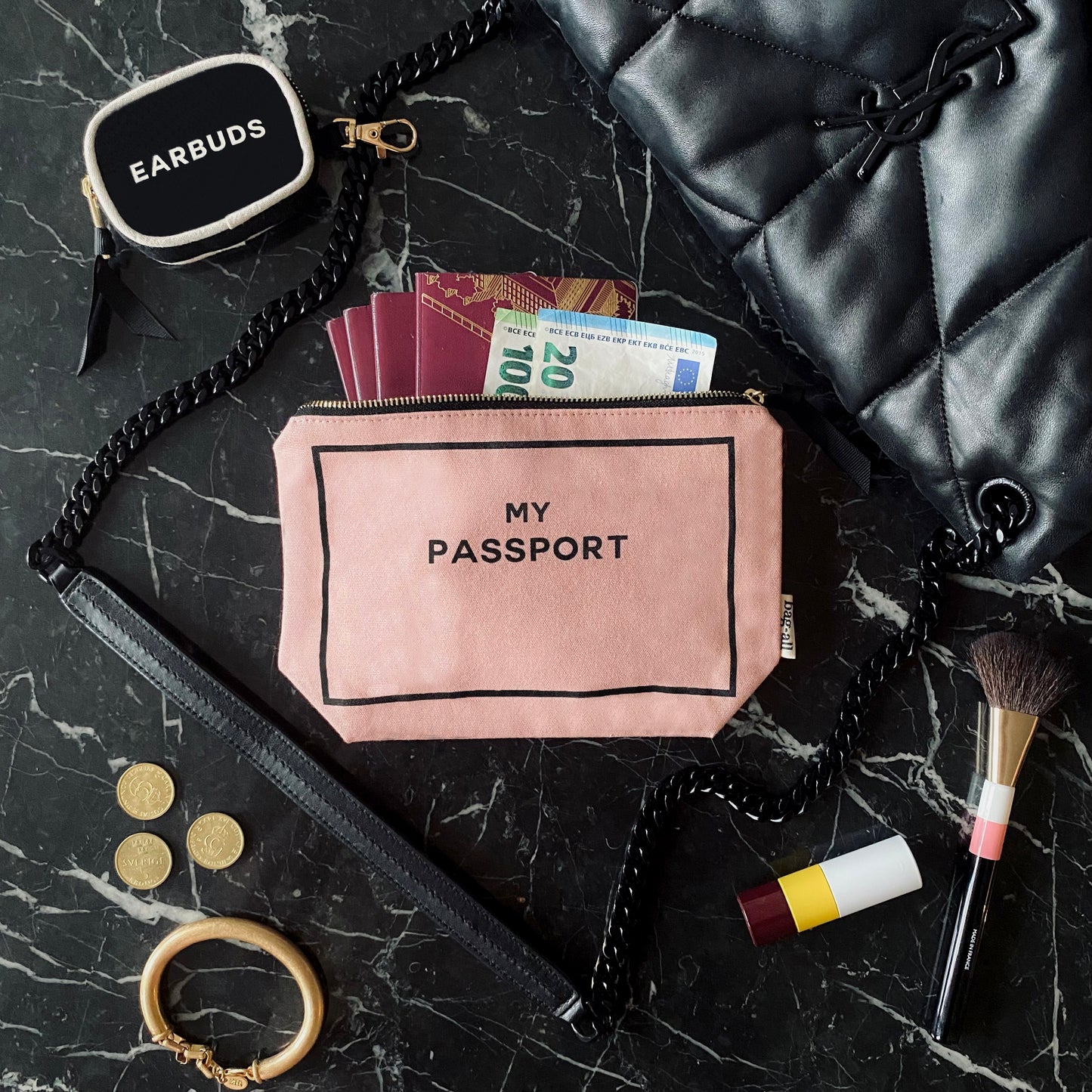 Bag-all pink passport organizer with cash and documents on marble surface with makeup and accessories nearby