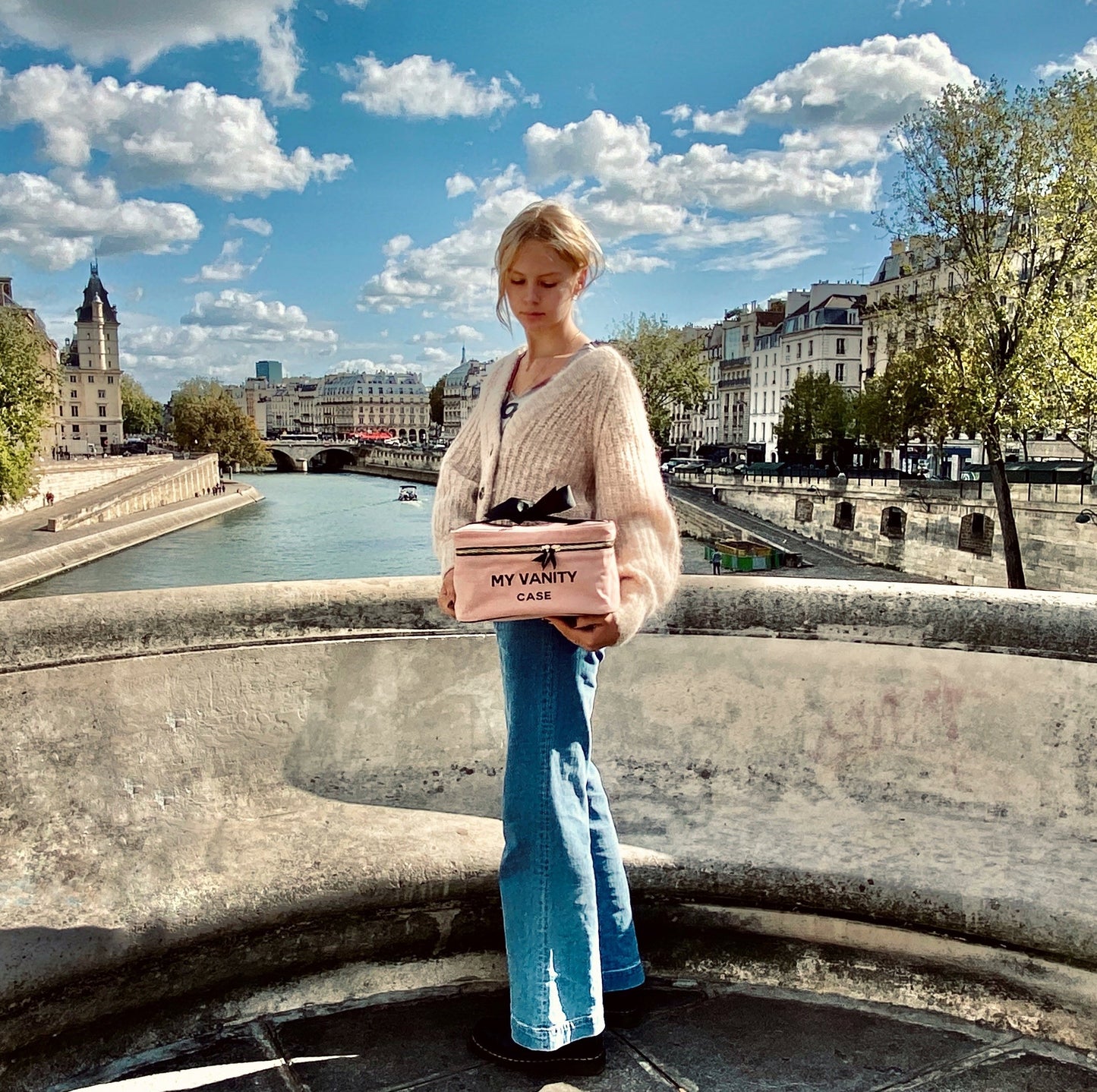 Bag-all My Vanity Large Beauty Box in pink/blush showcased on a scenic Paris bridge over the Seine River, featuring classic architecture and fluffy white clouds in a bright blue sky