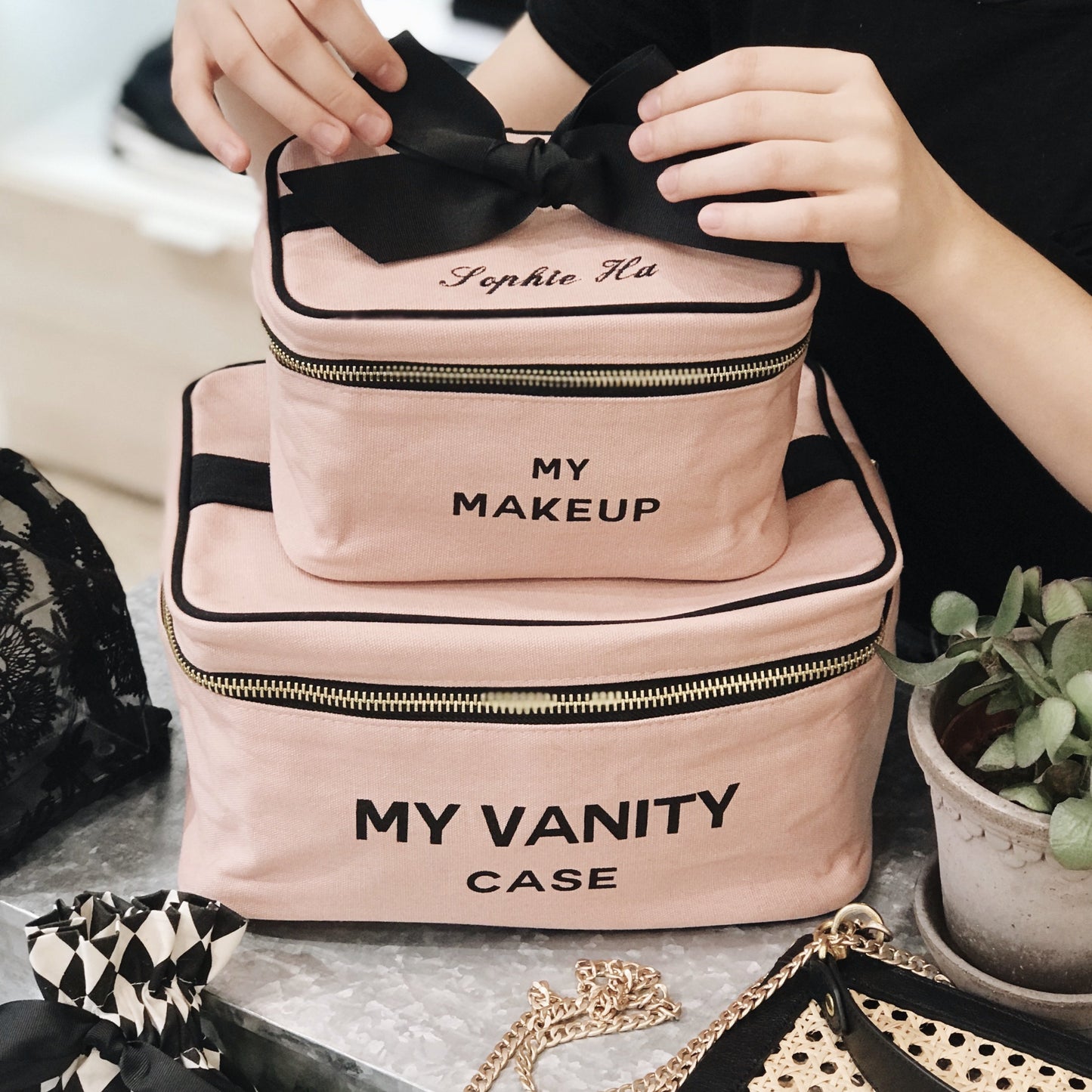 Bag-all My Makeup Cosmetic Box in blush pink with black bow, gold zipper, and black text. Stackable vanity organizer with laminated interior and carrying handle.