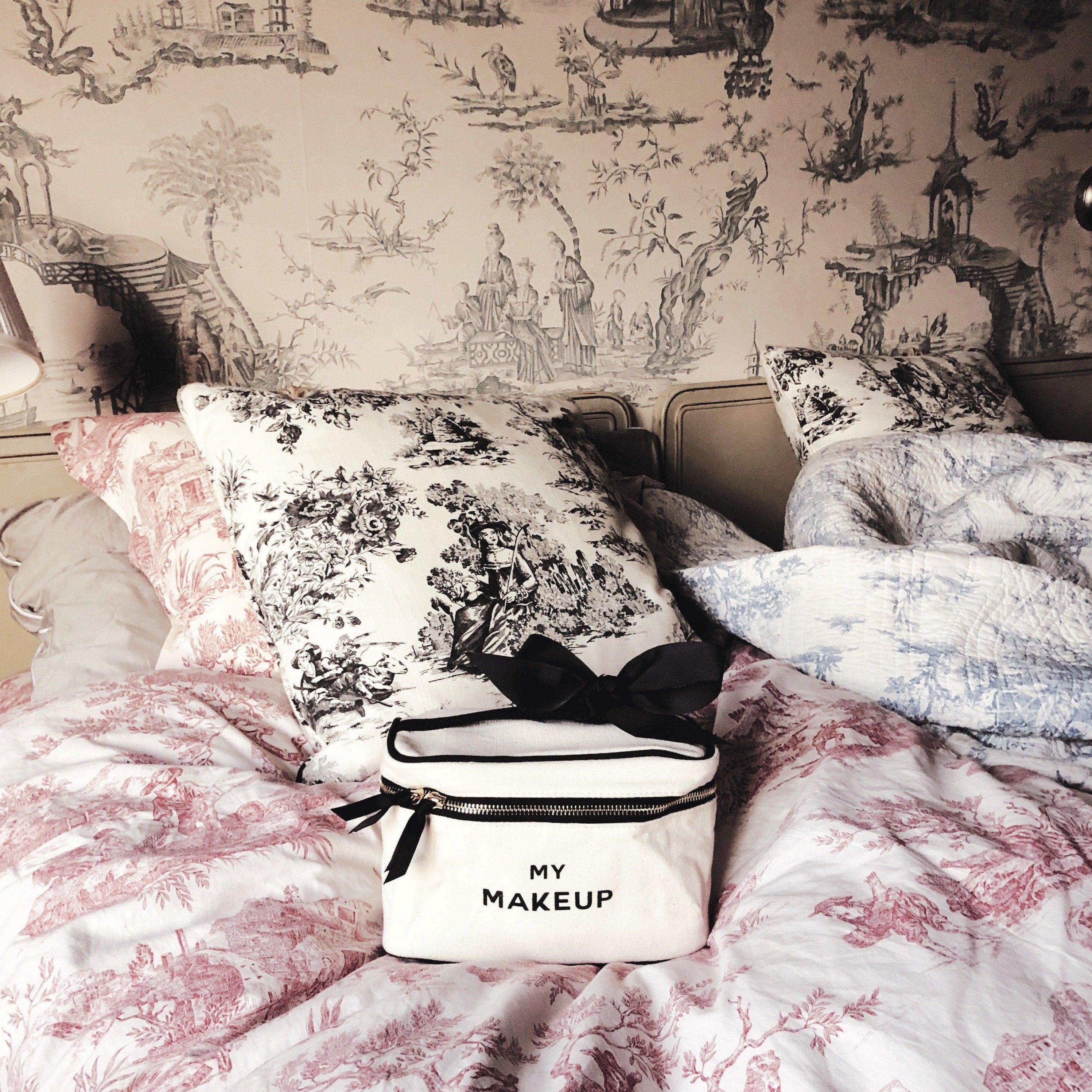 Bag-all My Makeup Cosmetic Box in cream color positioned on floral bedding, featuring black bow details and text, perfect for organized beauty storage and travel