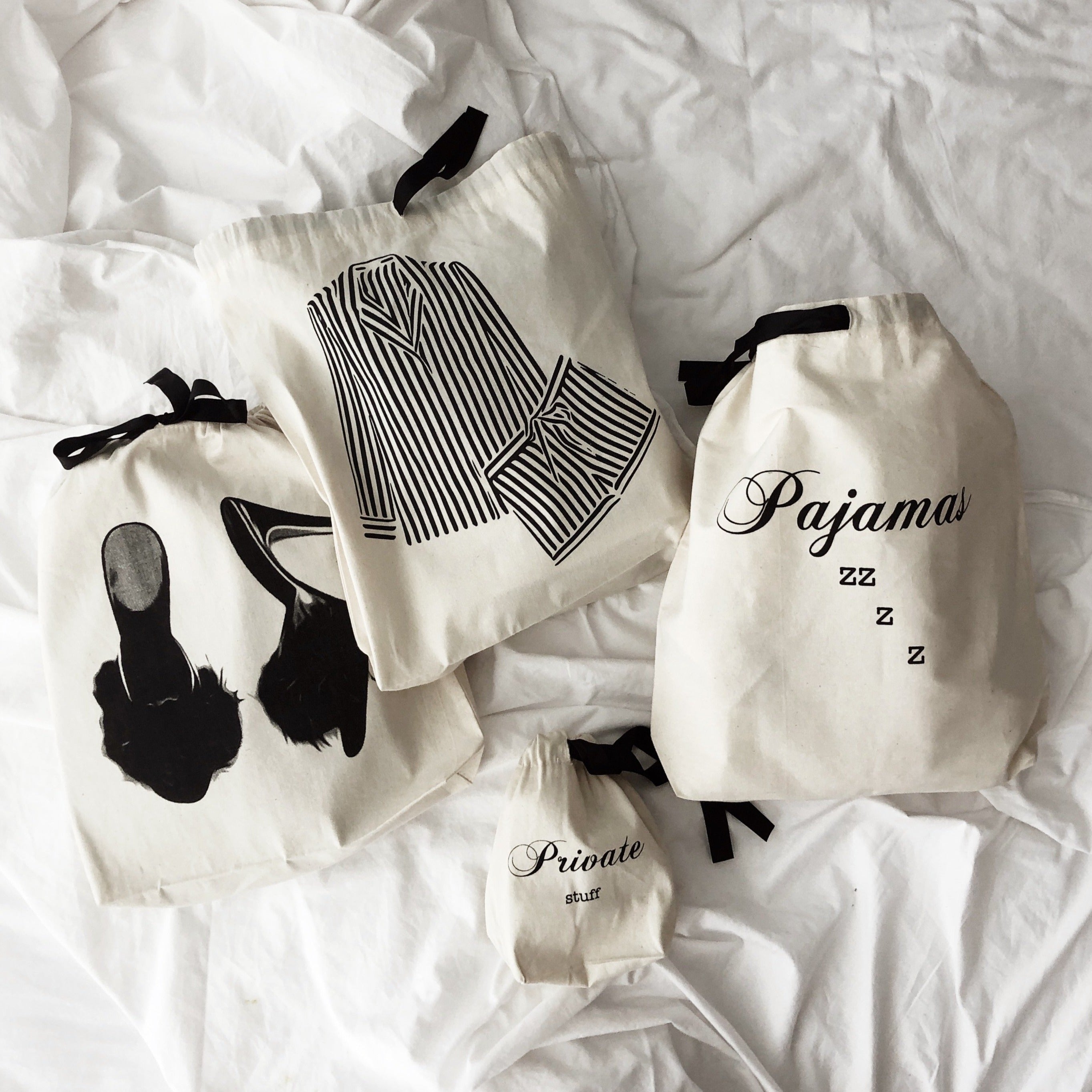 Bag-all Pajamas Zzzz Travel Bag in cream cotton with black drawstring, featuring stylish text design and hanging loop, shown with matching organizer bags for shoes and sleepwear