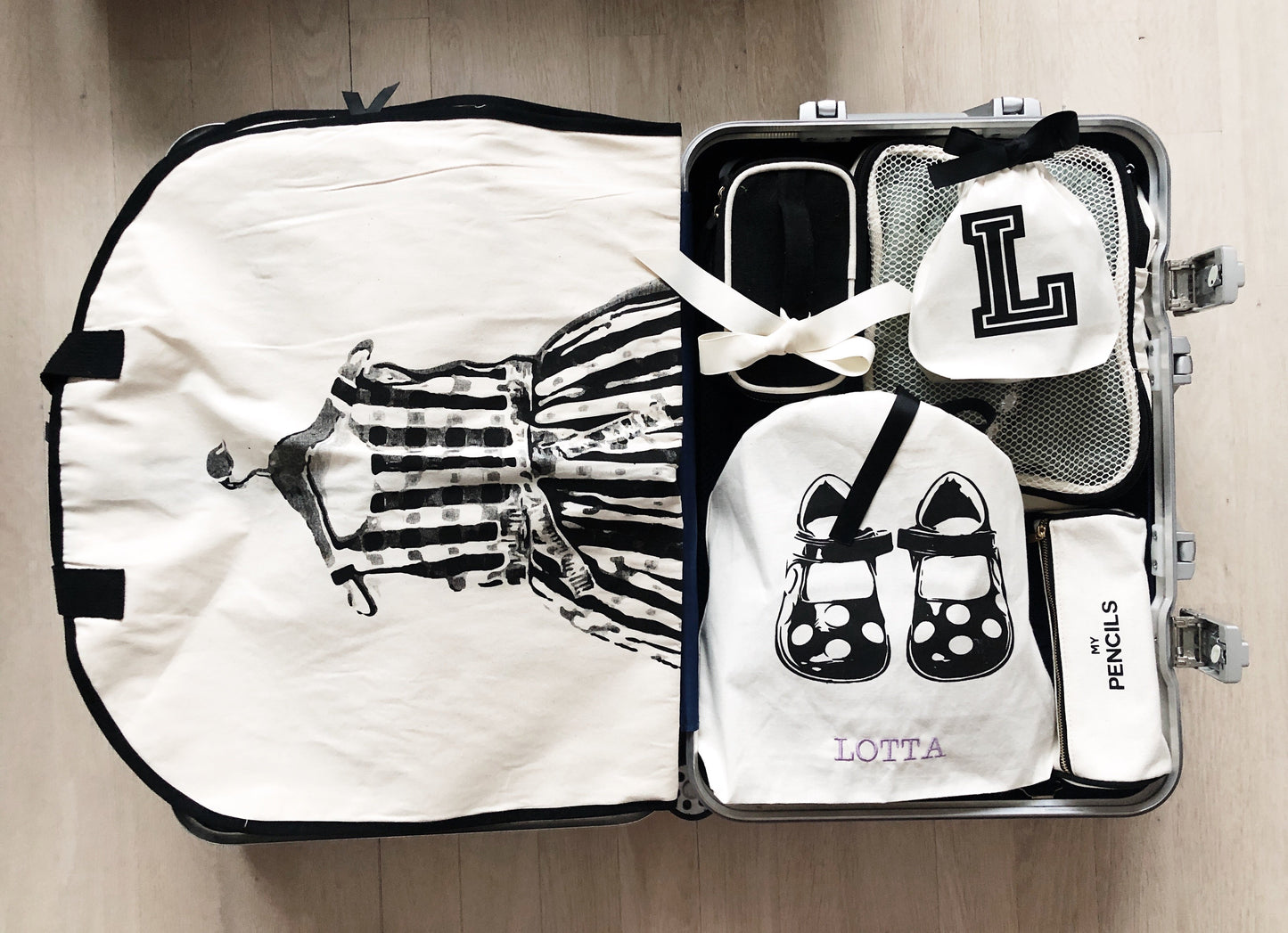 Bag-all Children Shoe Bag in cream with organizing compartments for shoes and socks, featuring black and white checkered dress illustration, displayed in open suitcase