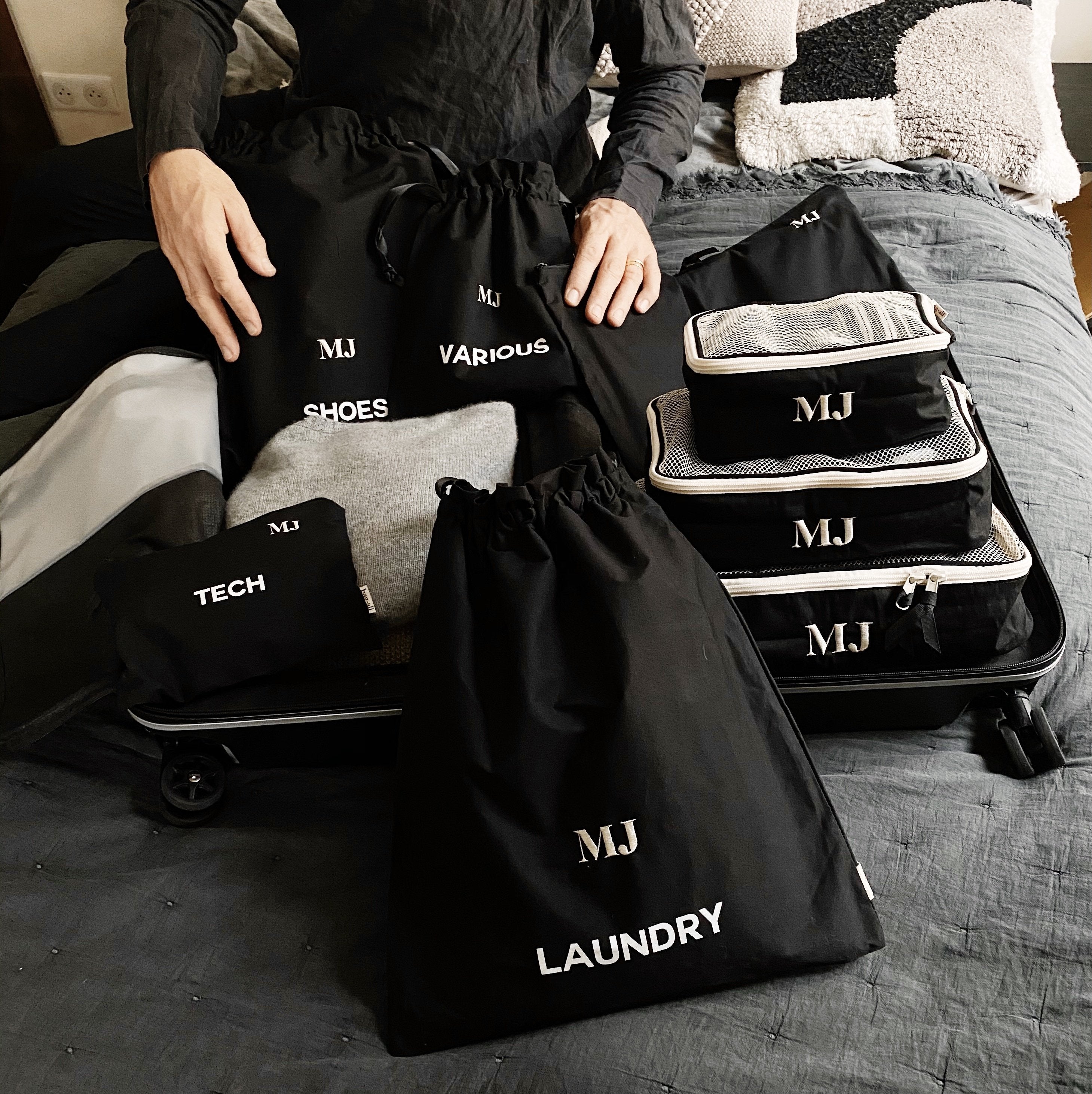 Bag-all personalized travel organizer set with black cotton bags and white monogram MJ, featuring compartments for shoes, tech, laundry and various items, perfect for organized packing