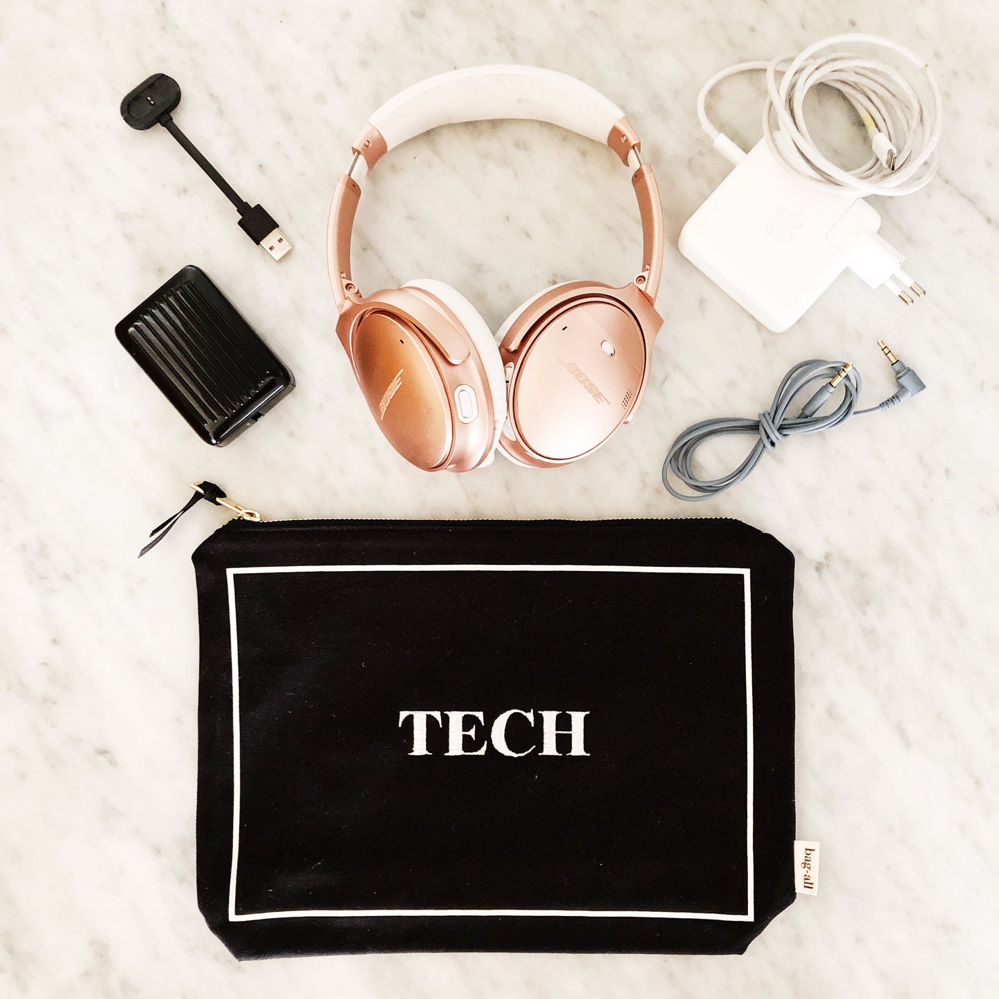 Bag-all Tech Pouch in Black with rose gold headphones, charger, and cables organized neatly on marble surface - perfect storage solution for electronic accessories and gadgets