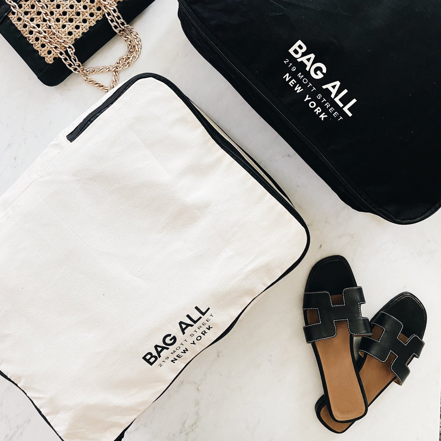 Bag-all Large Double Sided Packing Cube in cream with black trim, featuring dual compartments and shoe storage pocket, displayed with sandals and brand packaging.