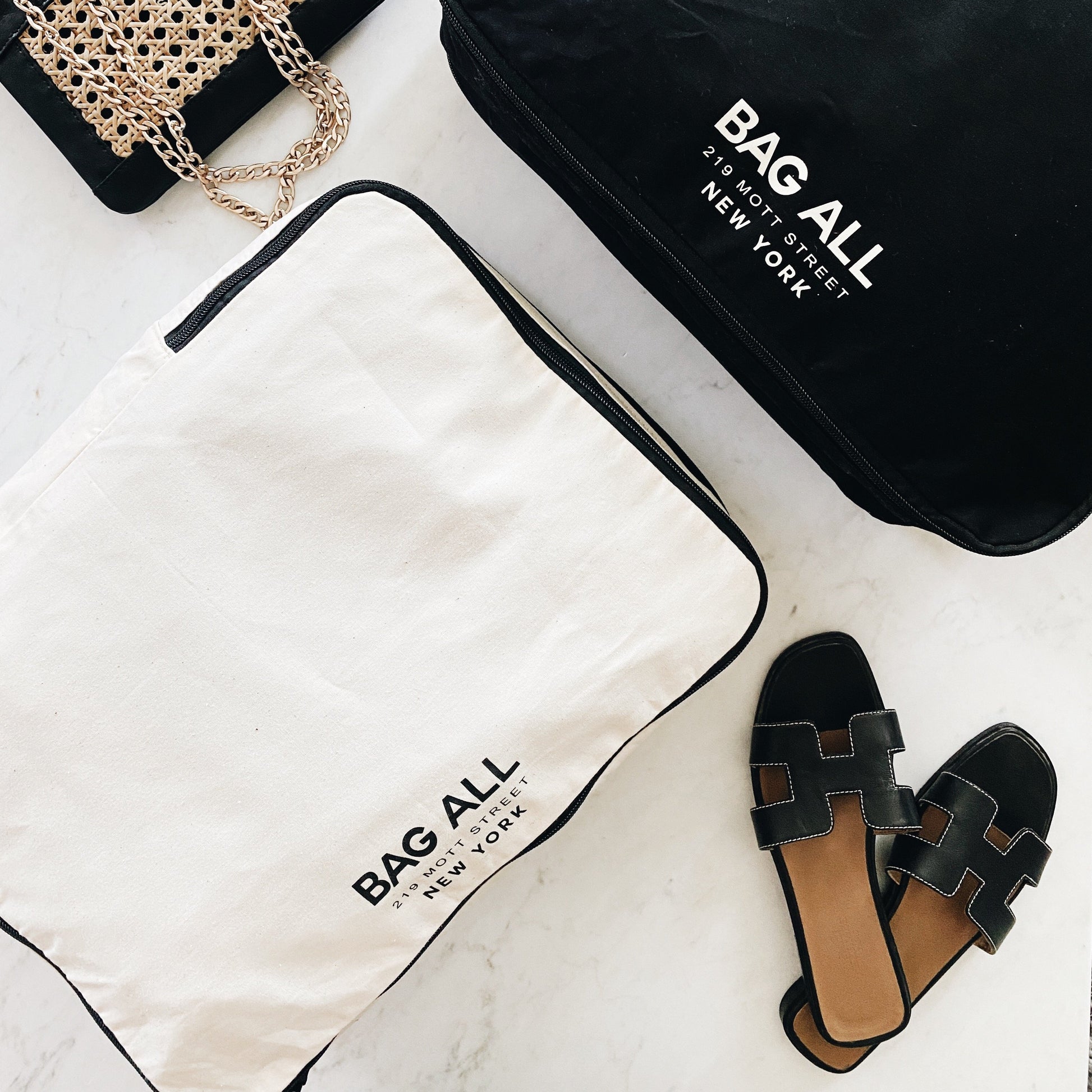Bag-all Large Double Sided Packing Cube in cream with black trim, featuring dual compartments and shoe storage pocket, displayed with sandals and brand packaging.