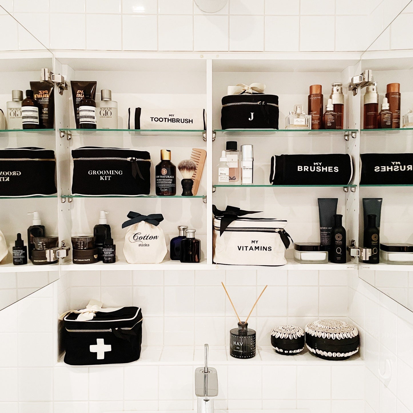 Bag-all Vitamins Storage and Travel Box in cream color displayed in an organized bathroom cabinet alongside black and white toiletry cases and grooming essentials on white tiled shelves