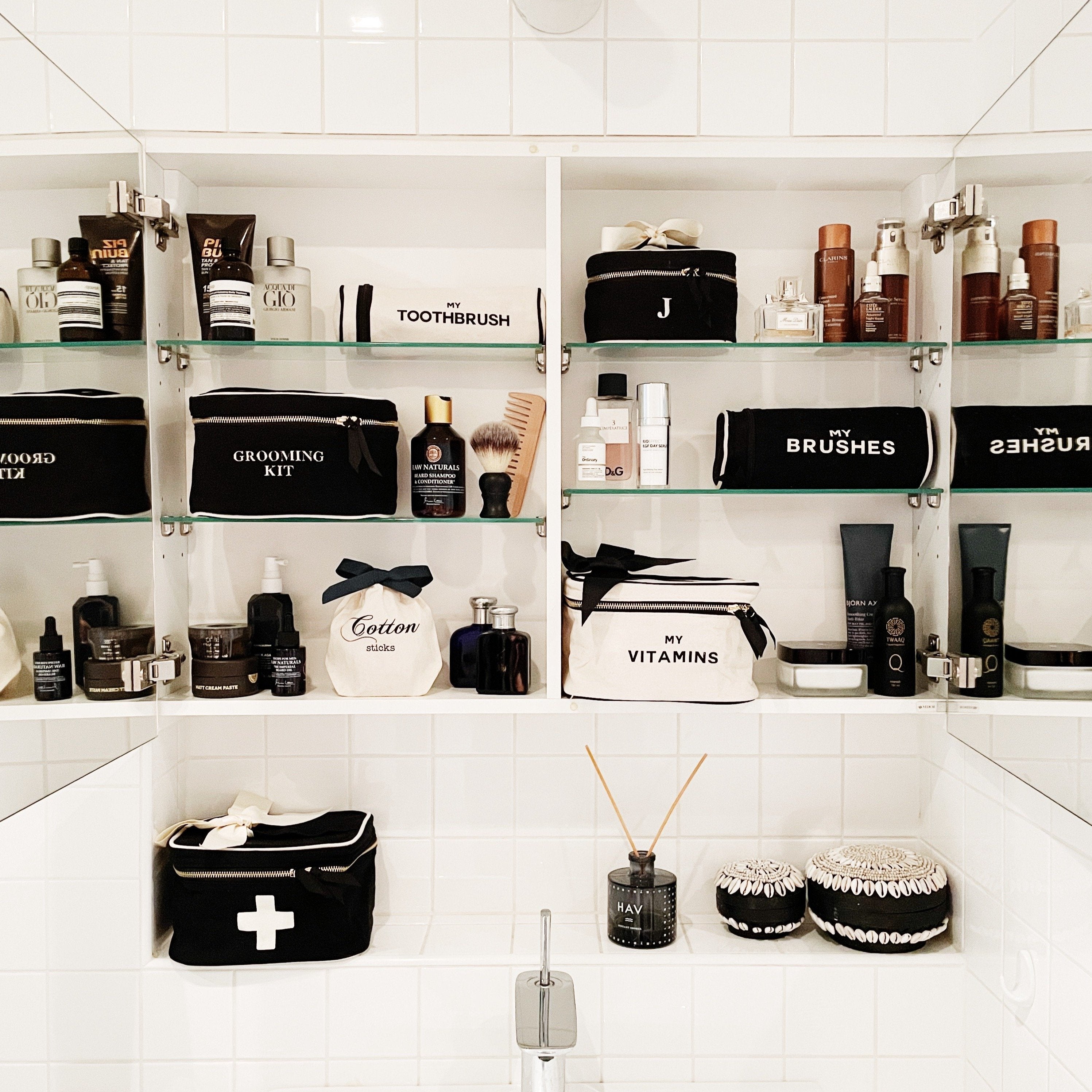 Bag-all Vitamins Storage and Travel Box in cream color displayed in an organized bathroom cabinet alongside black and white toiletry cases and grooming essentials on white tiled shelves