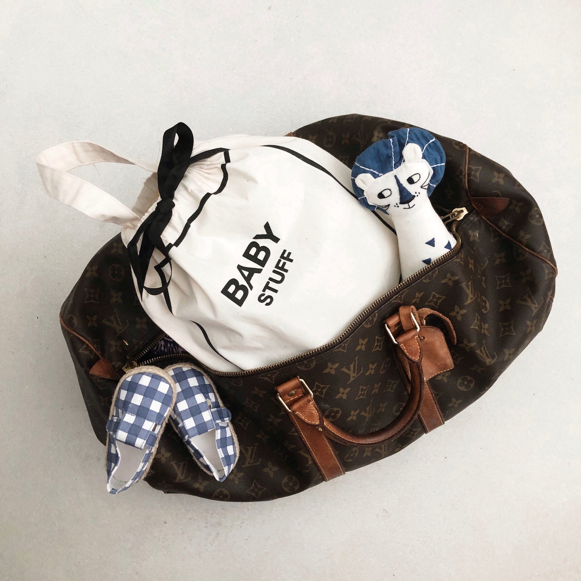 Bag-all Baby Stuff organizer bag in luxe travel duffle, featuring blue gingham bunny slippers and matching bow accessories, perfect for stylish baby essentials storage