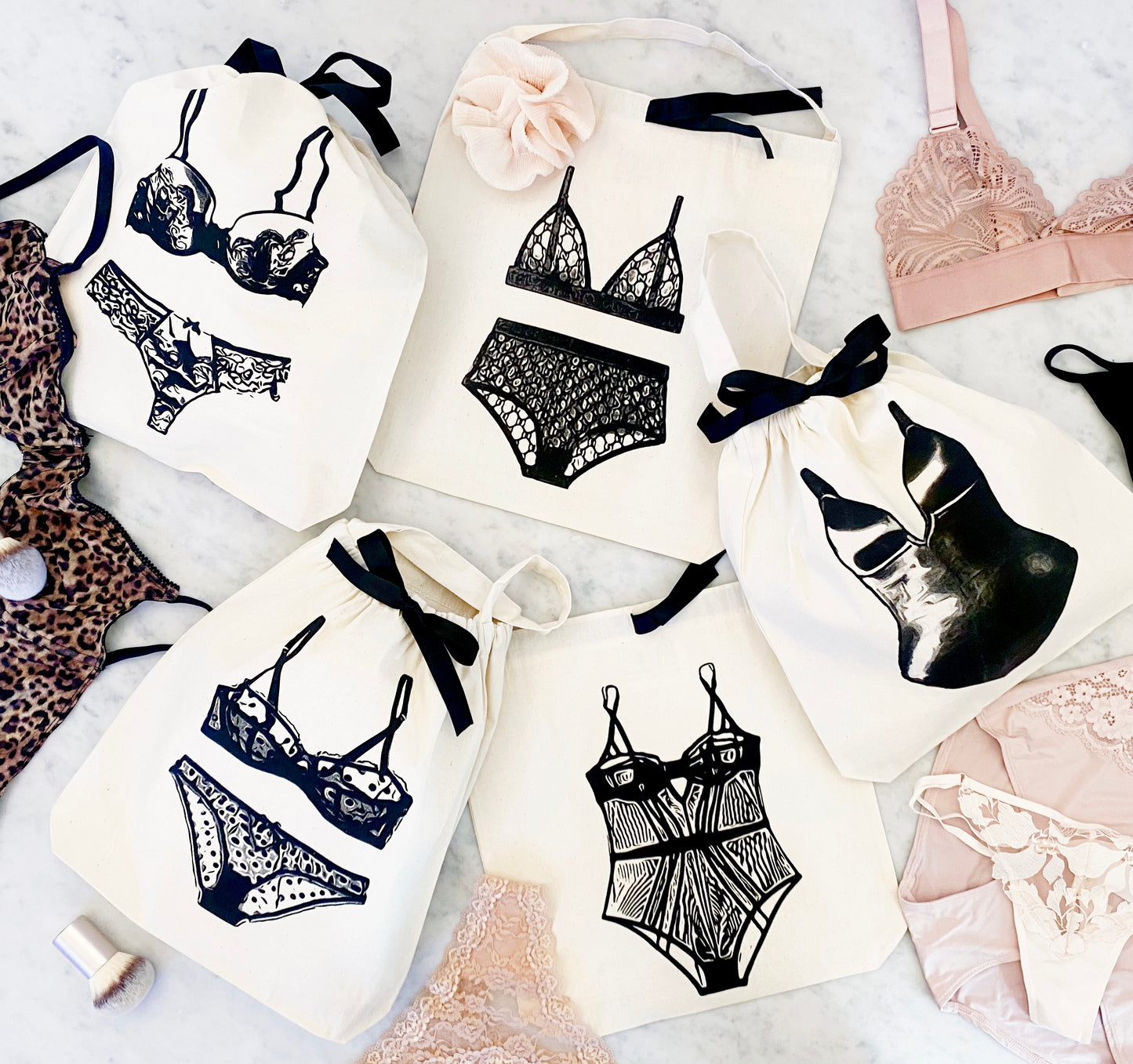 Bag-all London Lingerie Travel Bag in cream with black lingerie illustrations featuring delicate lace bras and panties on cotton storage pouches with ribbon ties