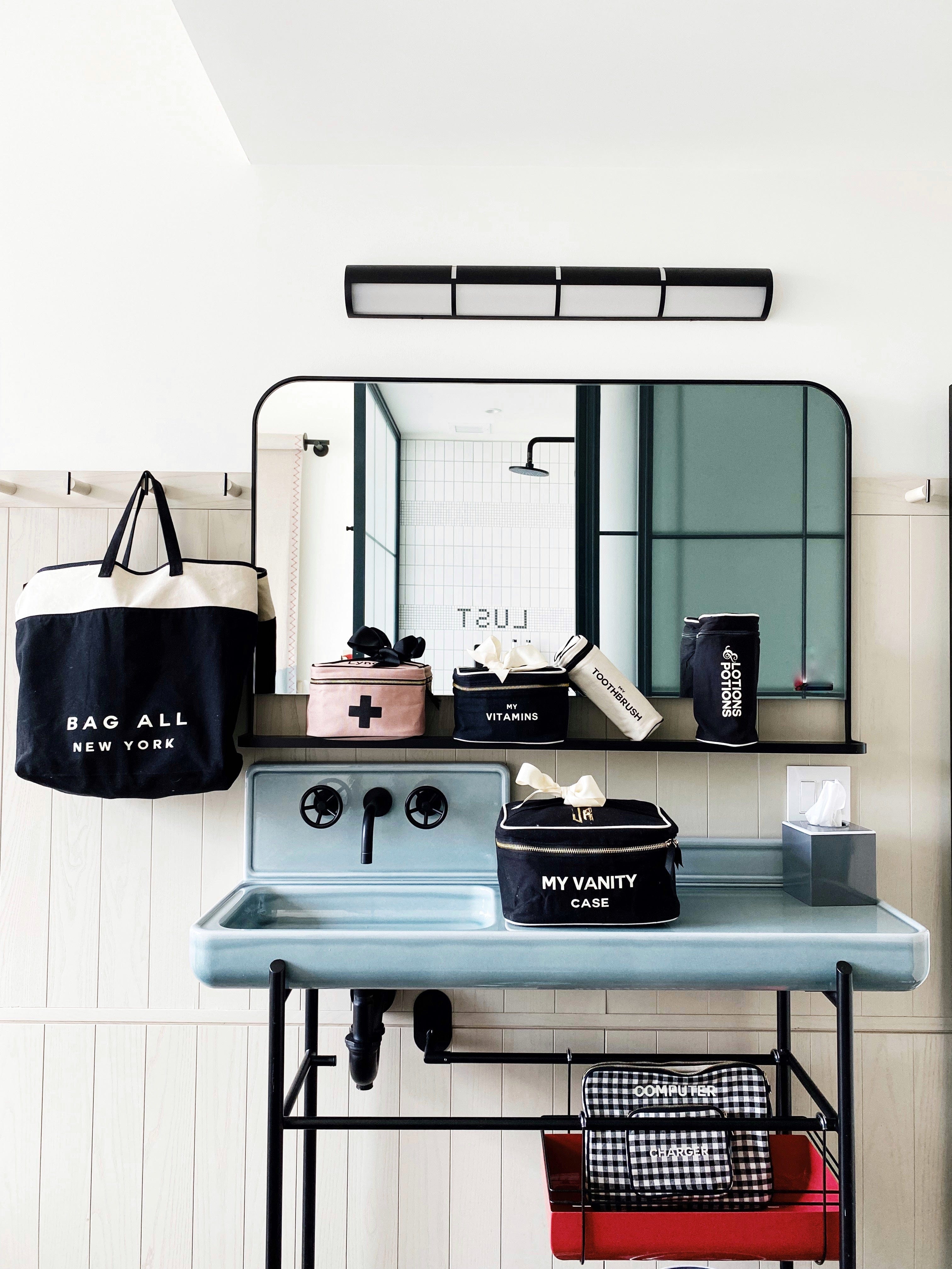 Bag-all Pink First Aid Storage Box with black cross print, shown with other organizing cases in a modern bathroom setting, featuring eco-friendly cotton and striped interior lining