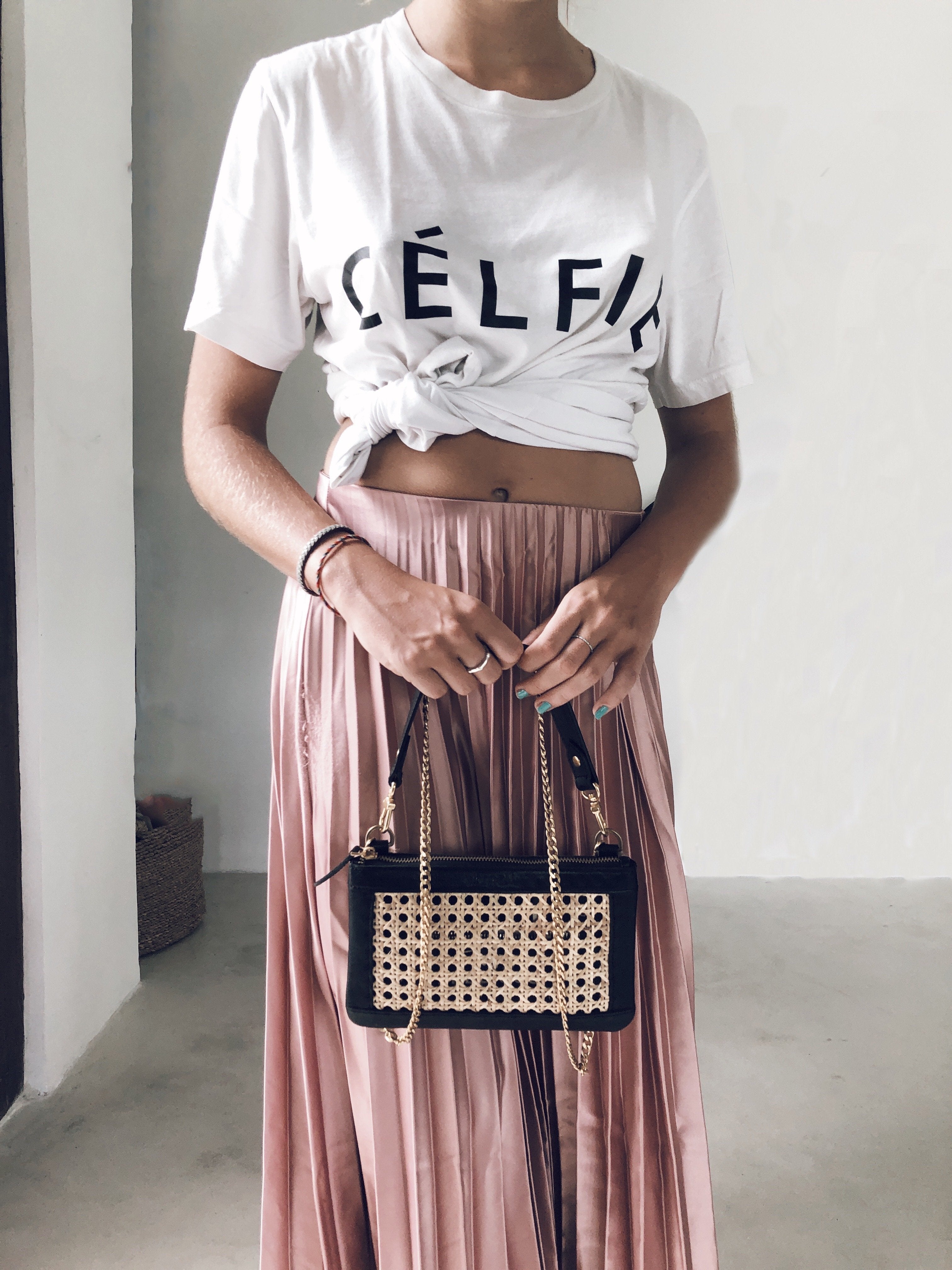 Bag-all Gold Chain removable strap accessory shown with stylish black handbag featuring woven rattan detail, paired with pink pleated skirt and white graphic tee