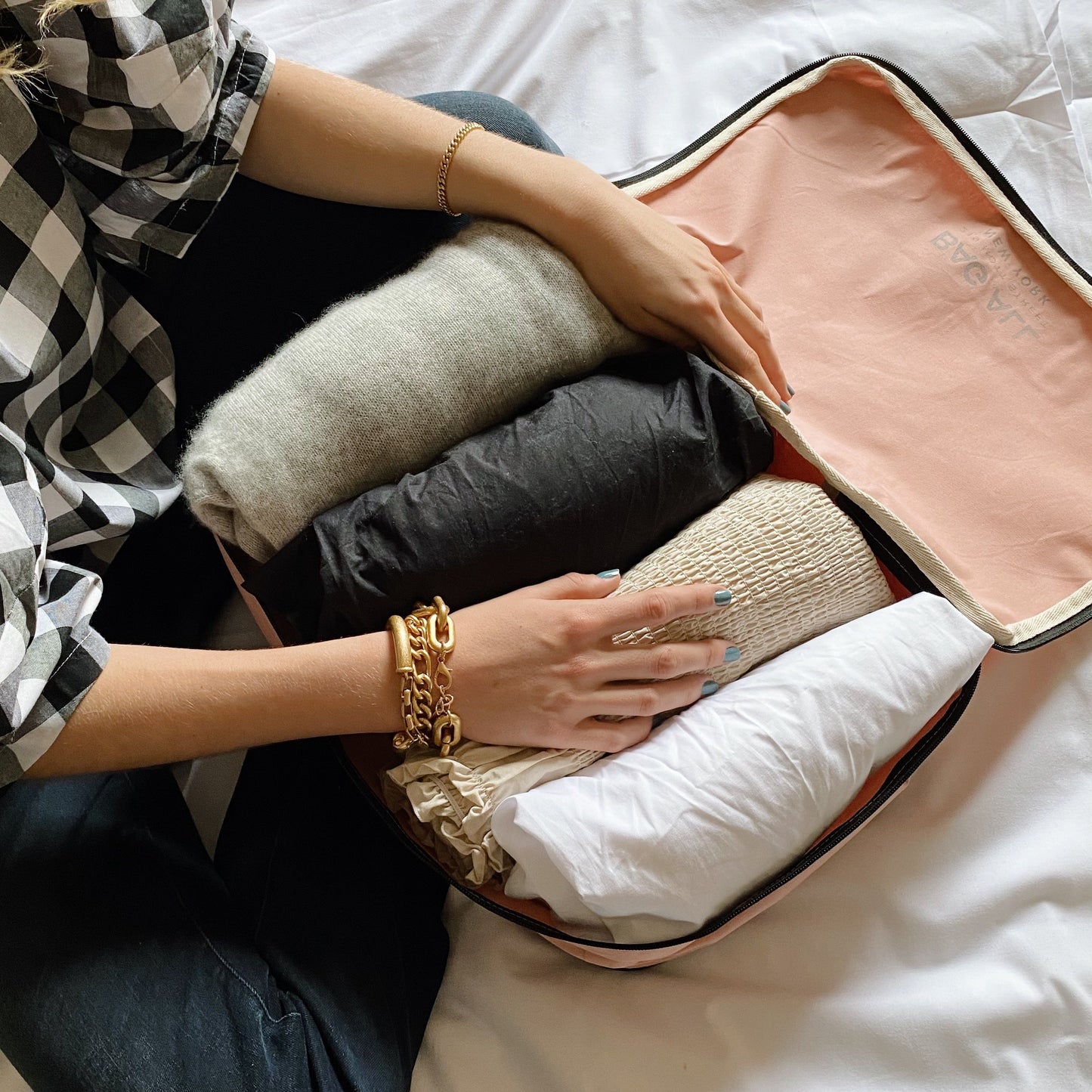 Bag-all Large Double Sided Packing Cube in Pink/Blush shown organizing rolled clothes in two compartments, featuring black trim and handle, displayed on white bedding