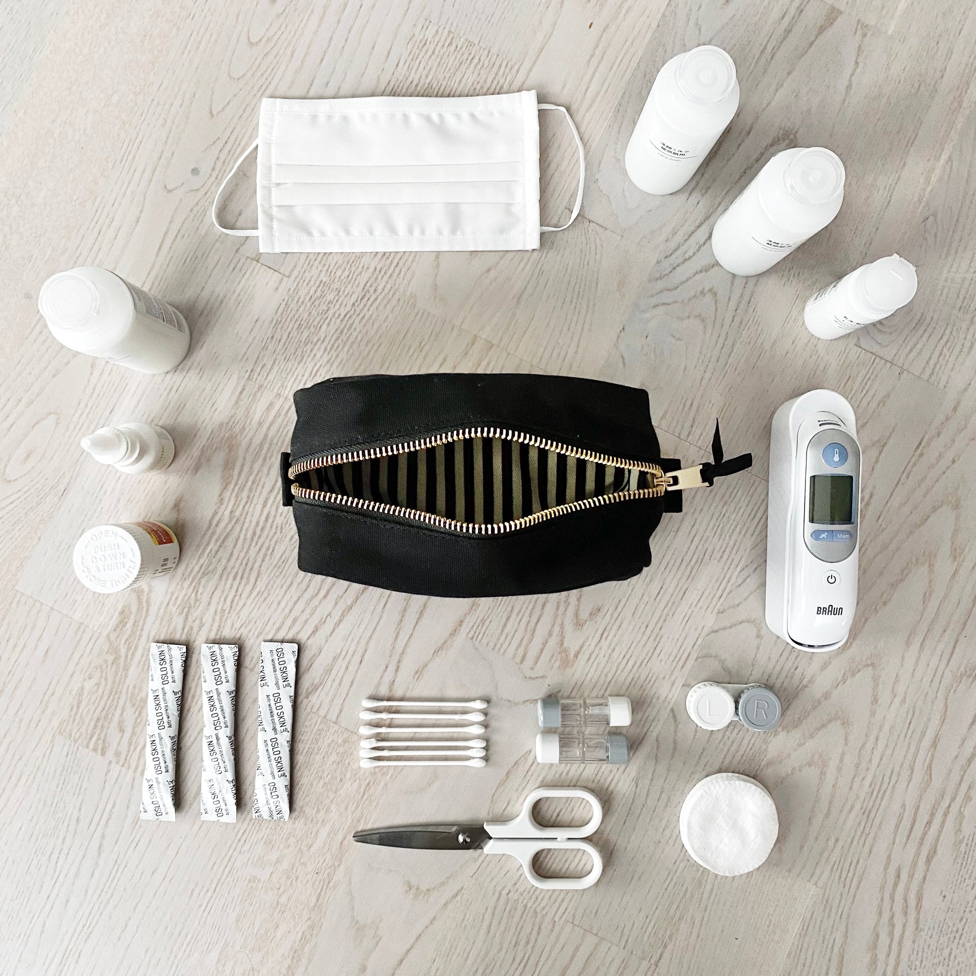 Bag-all First Aid Organizing Pouch in black cotton with striped interior lining, displayed with medical essentials including thermometer, masks, and bandages on light wooden surface