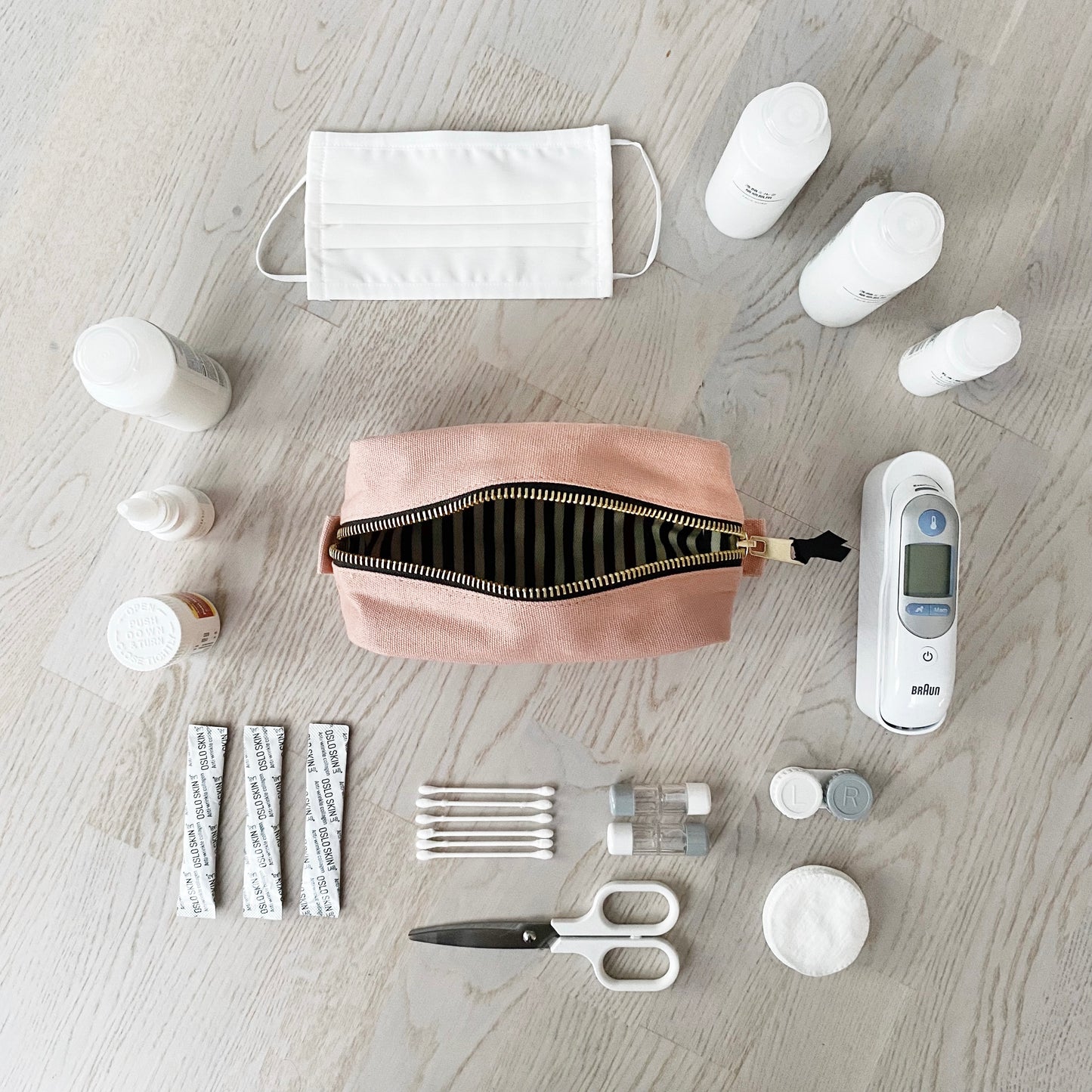 Bag-all First Aid Organizing Pouch in blush pink shown with medical essentials including face mask, thermometer, medicine bottles, bandages, and scissors arranged neatly on wooden surface