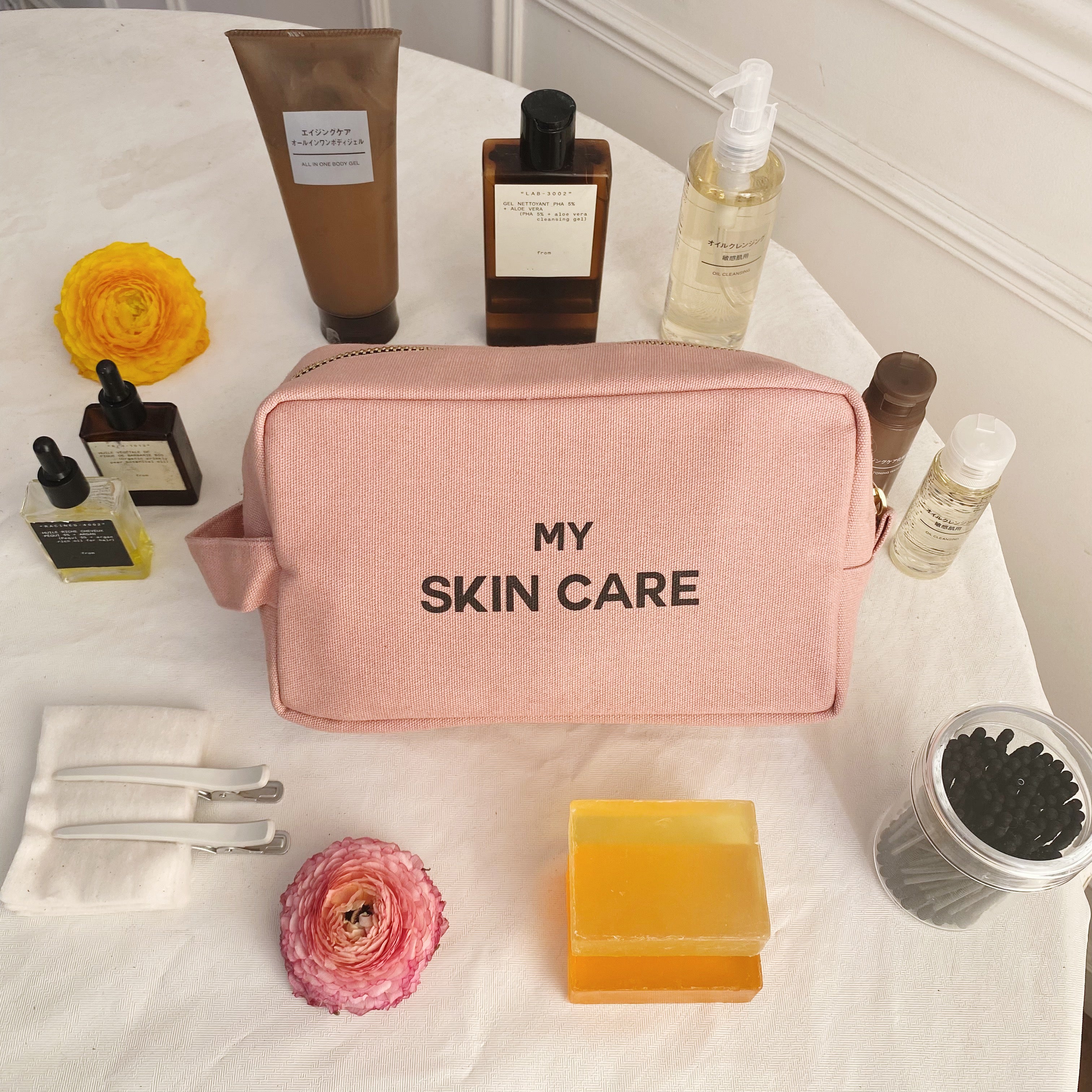 Bag-all My Skin Care Organizing Pouch in blush pink cotton with waterproof lining, displayed with skincare products, flowers, and beauty essentials on white surface