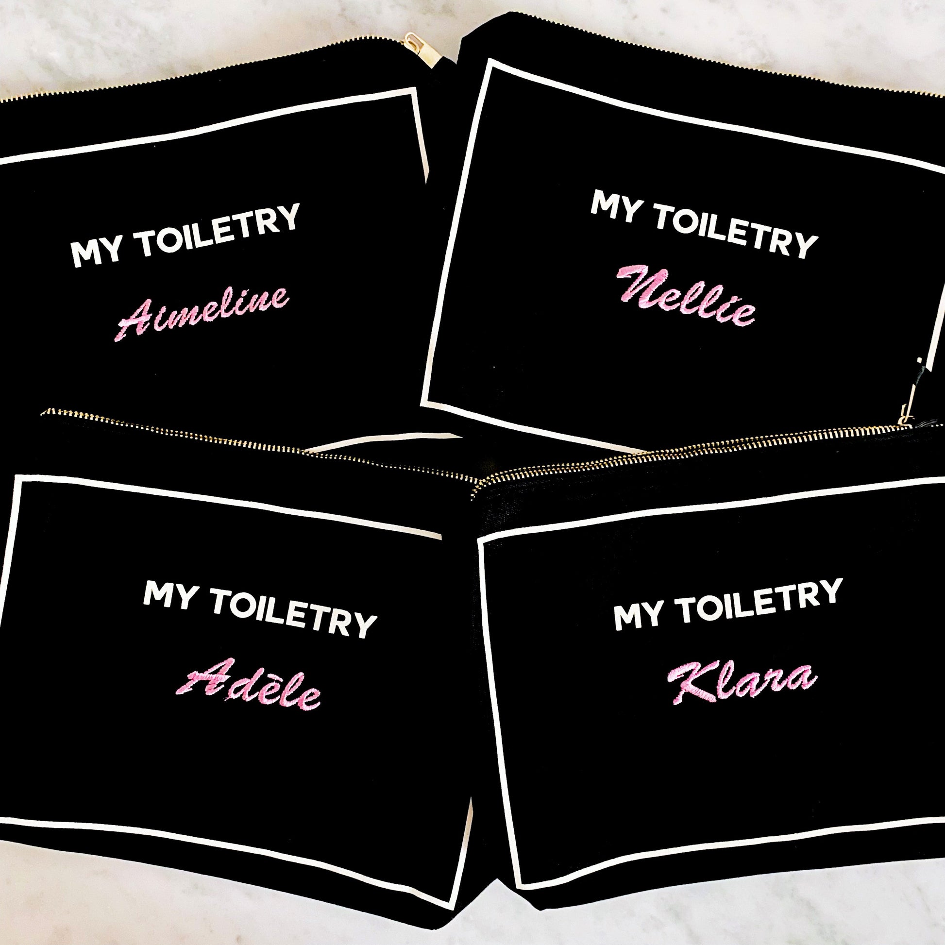 Bag-all Black Toiletry Pouch with Coated Lining featuring personalized names in pink script, showcasing four matching organizer bags with metal zippers and white trim details