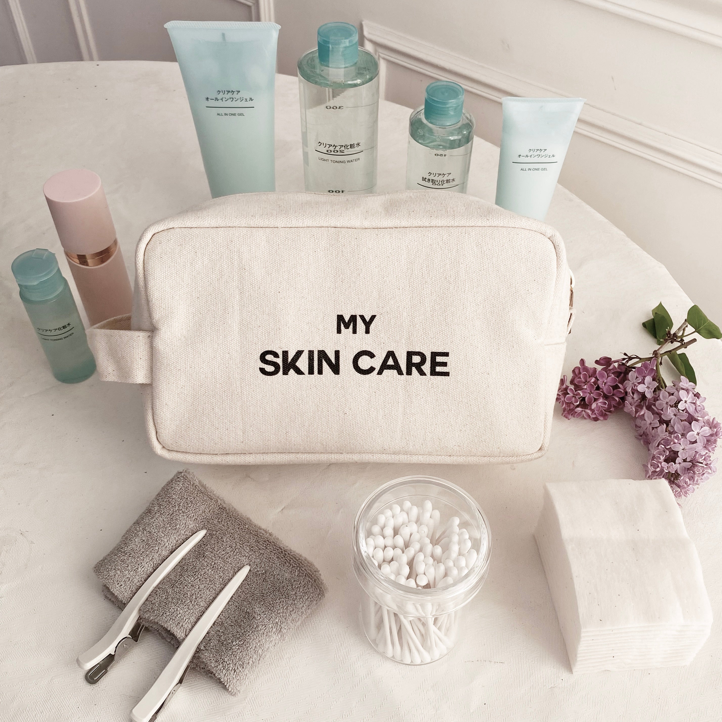 Bag-all My Skin Care Organizing Pouch in natural cotton with waterproof lining, shown with skincare products, cotton swabs and lilac flowers in a minimalist bathroom setting