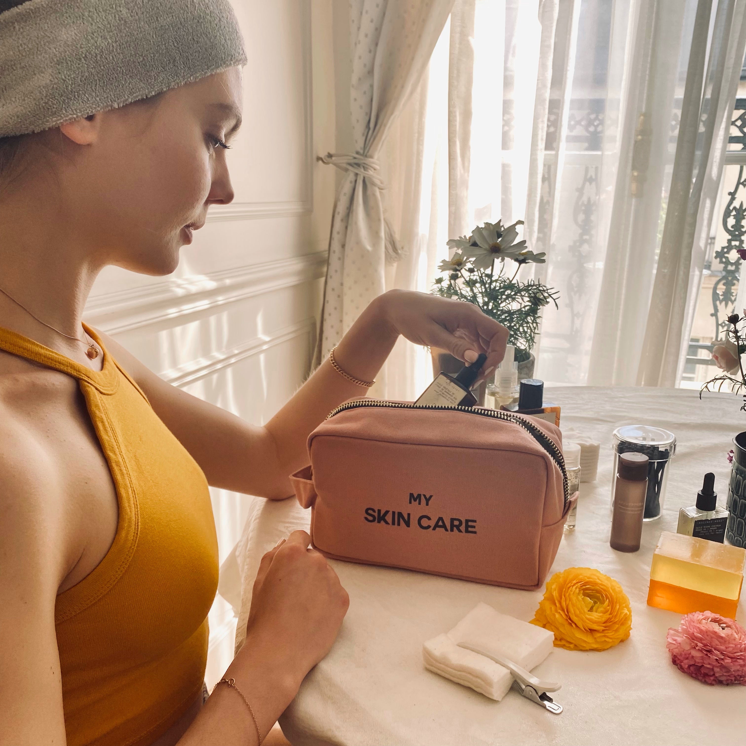 Bag-all My Skin Care Organizing Pouch in Pink/Blush, featuring waterproof lining and cotton construction, shown with skincare products on white vanity near window with natural light