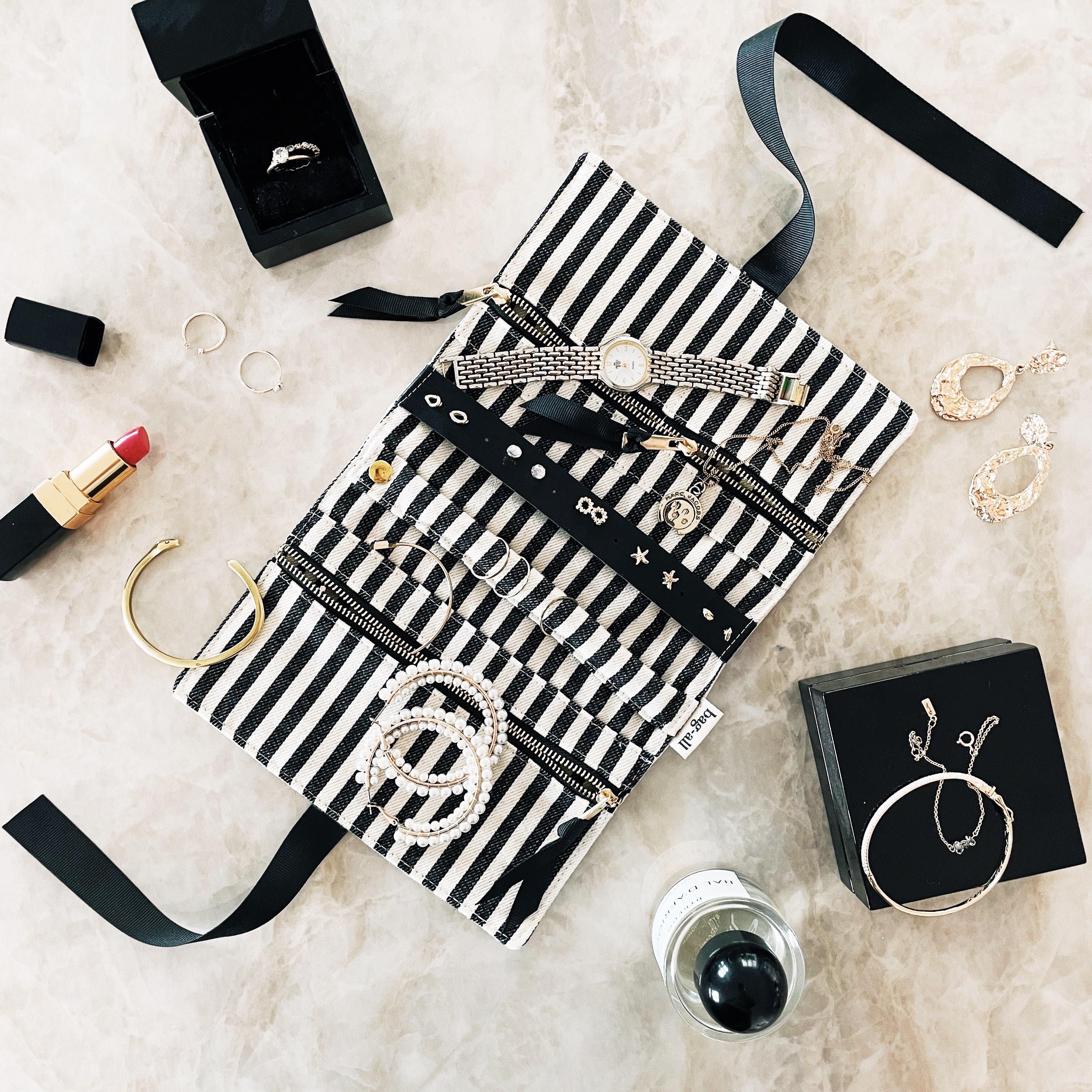 Bag-all Jewelry Organizer Travel Pouch in cream with black and white striped pattern, featuring multiple compartments, leather earring holder, and ring storage displayed with jewelry accessories