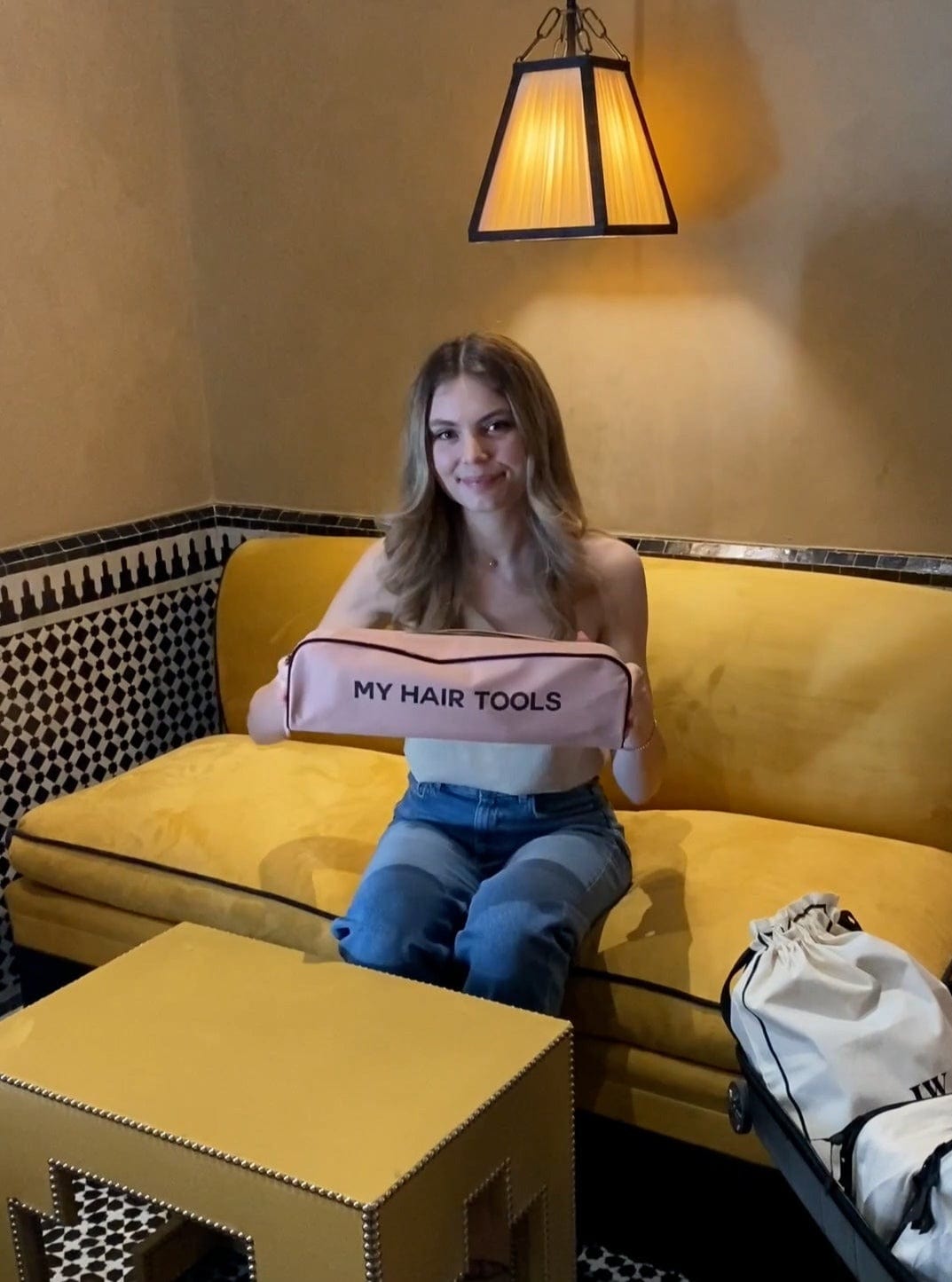 Bag-all Roomy Hair Tools Travel Case in pink blush shown on yellow couch, featuring spacious design and 'MY HAIR TOOLS' text, perfect for organizing styling tools and Airwrap