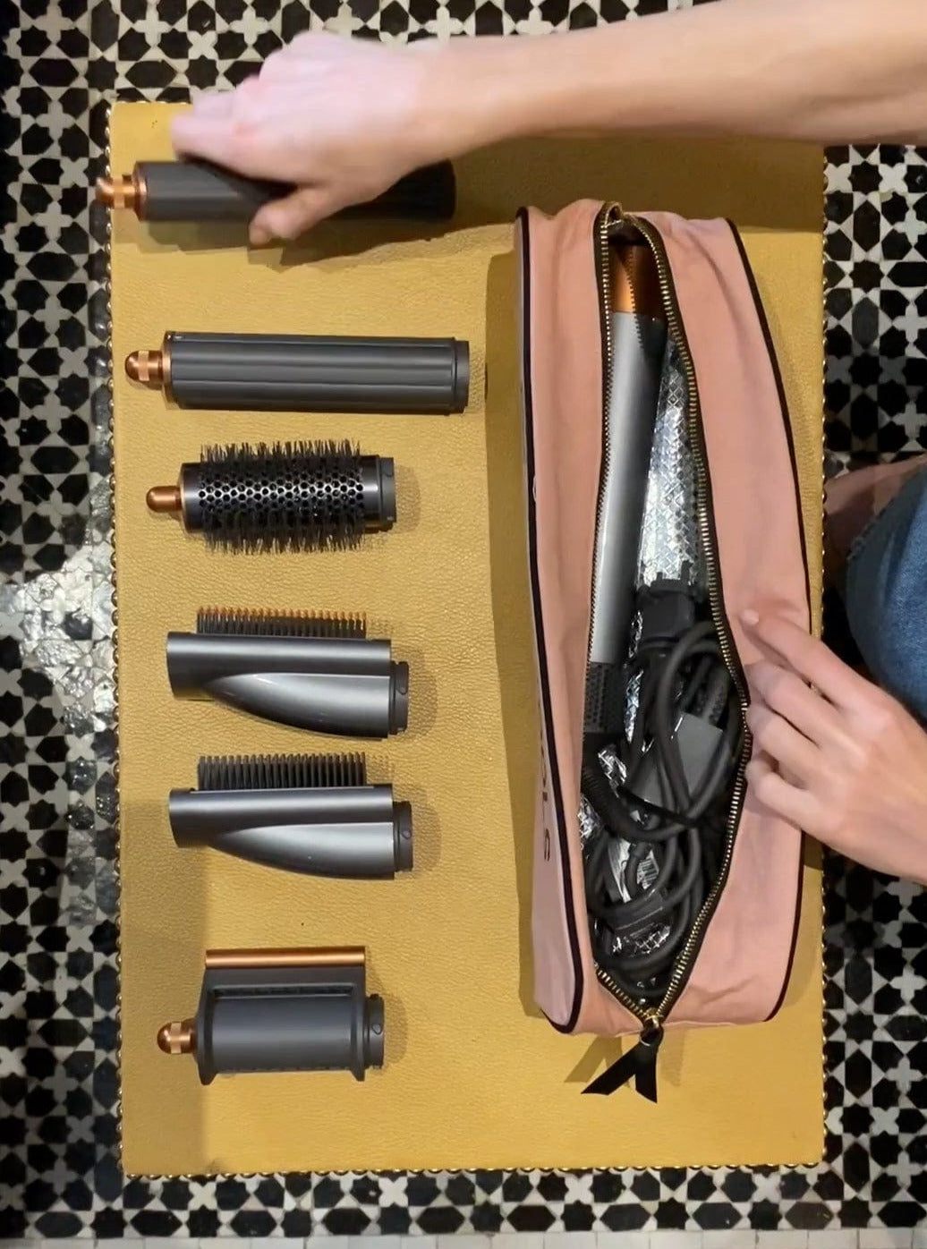 Bag-all Roomy Hair Wrap Tools Travel Case in pink blush shown with hair styling attachments and heat-resistant lining, featuring gold zipper on yellow surface