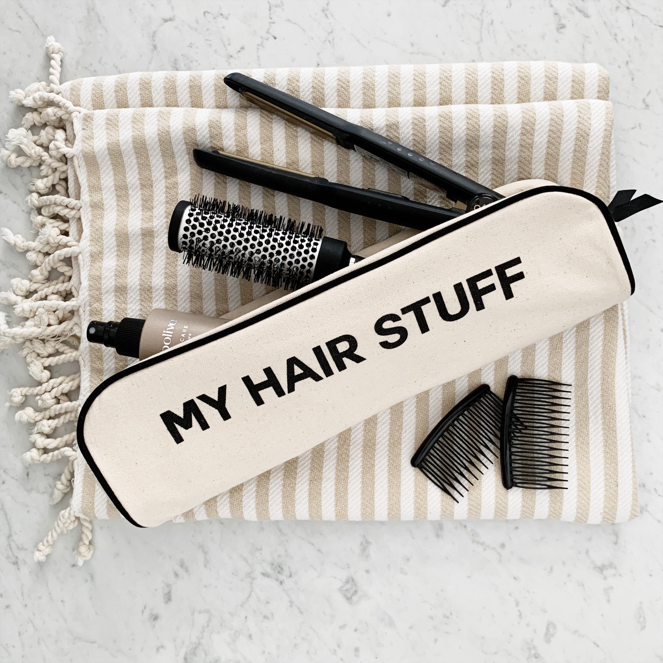 Bag-all Hair Stuff Travel Case in cream with black text on striped cotton background, shown with hair styling tools including brush, combs and styling implements, heat-resistant organizing case