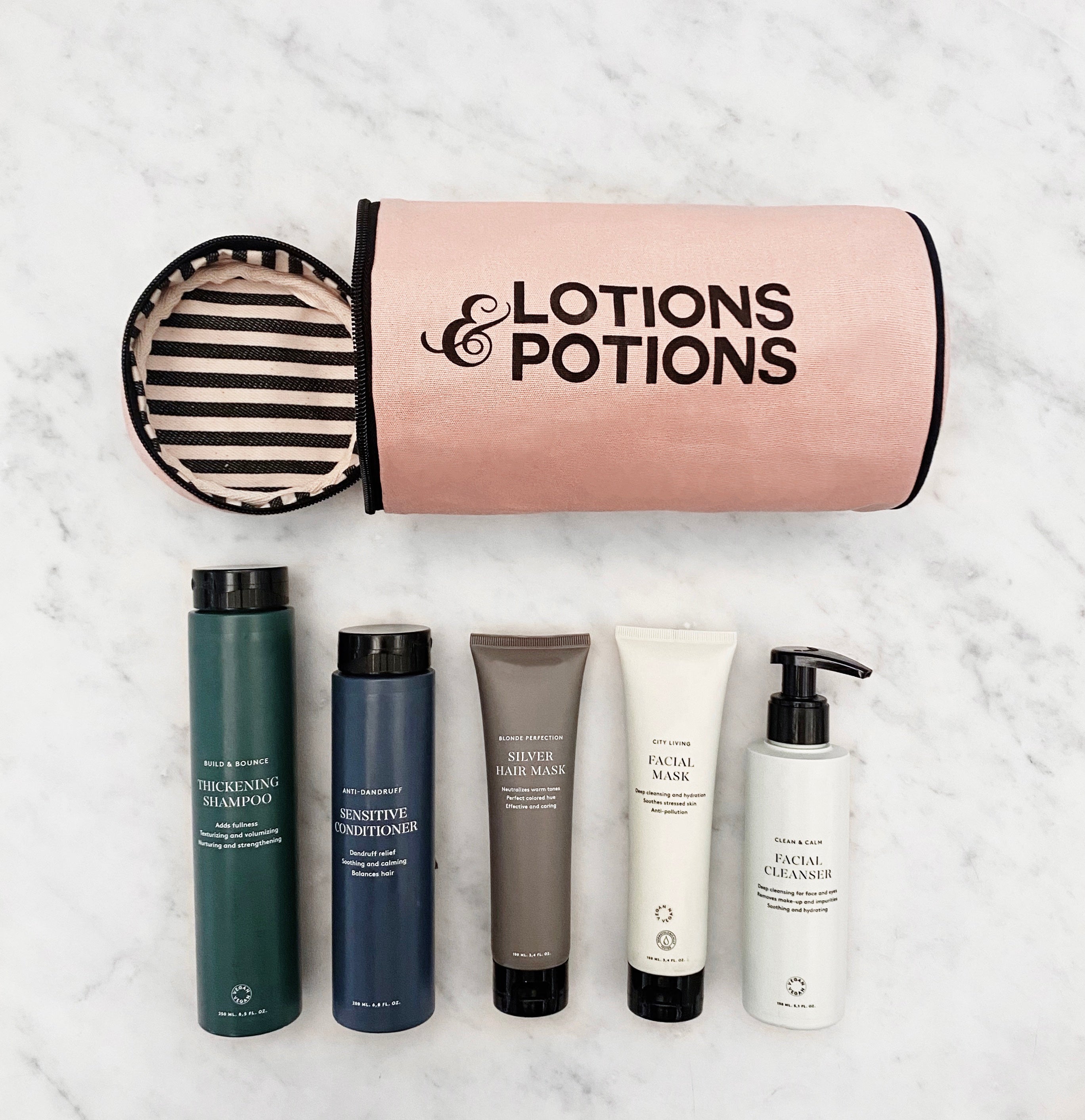 Bag-all Lotions & Potions Travel Case in blush pink with striped lining, shown with toiletry bottles on marble surface, perfect for organizing beauty essentials