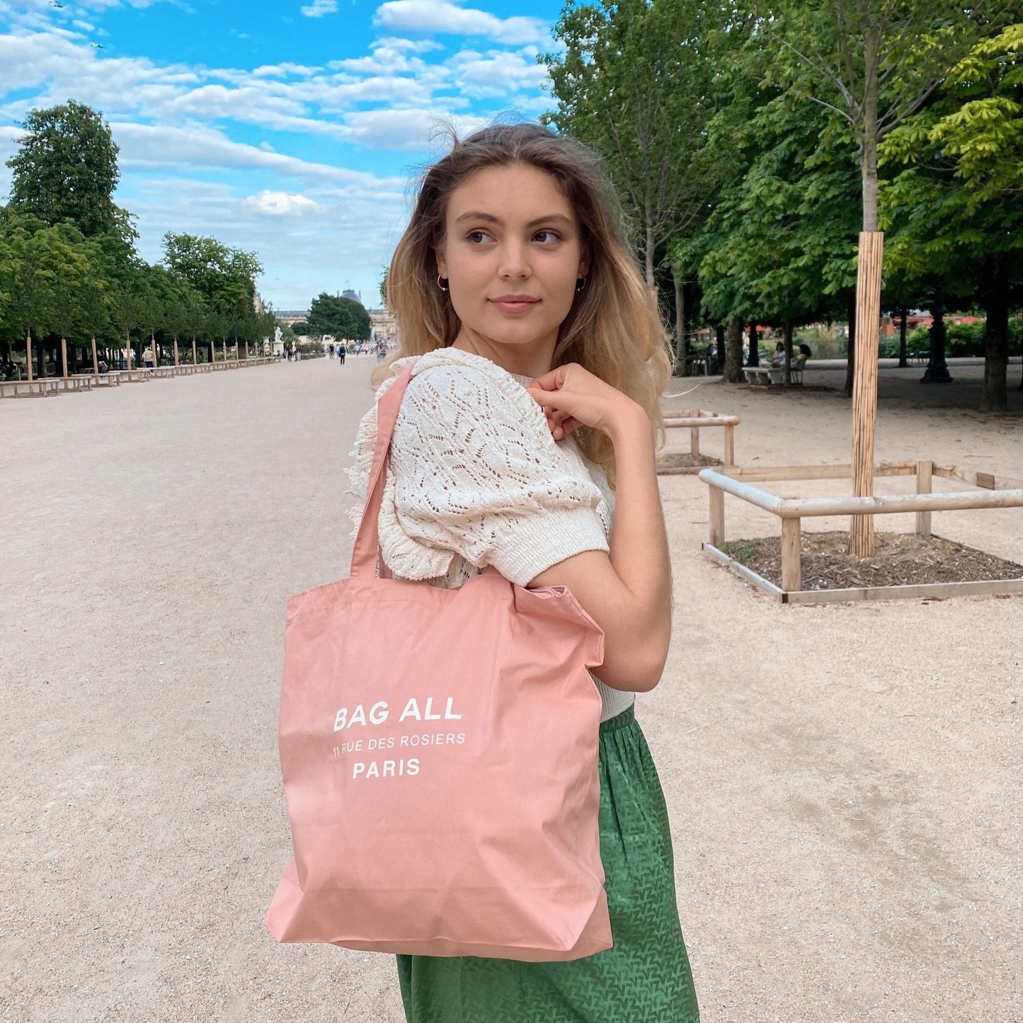 Bag-all Paris Le Marais Tote in blush pink cotton with zipper closure and interior pocket, shown in a park setting with trees and pathways. Perfect everyday carry with classic design.