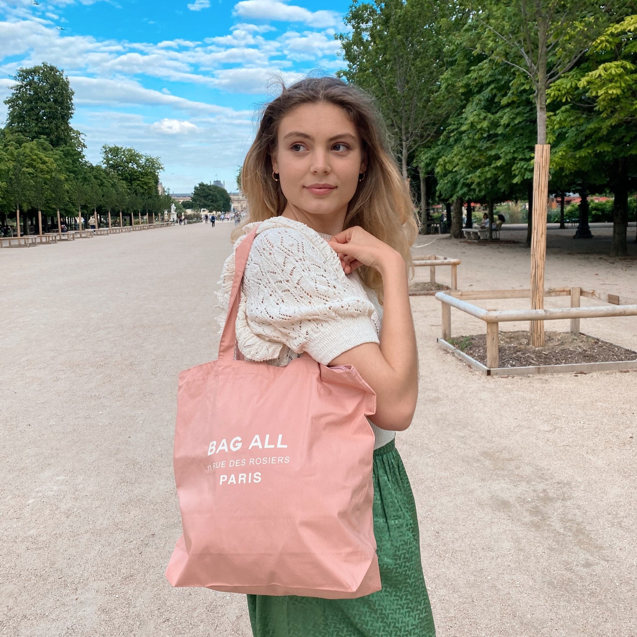 Bag-all Paris Le Marais Tote in blush pink cotton with zipper closure and interior pocket, shown in a park setting with trees and pathways. Perfect everyday carry with classic design.