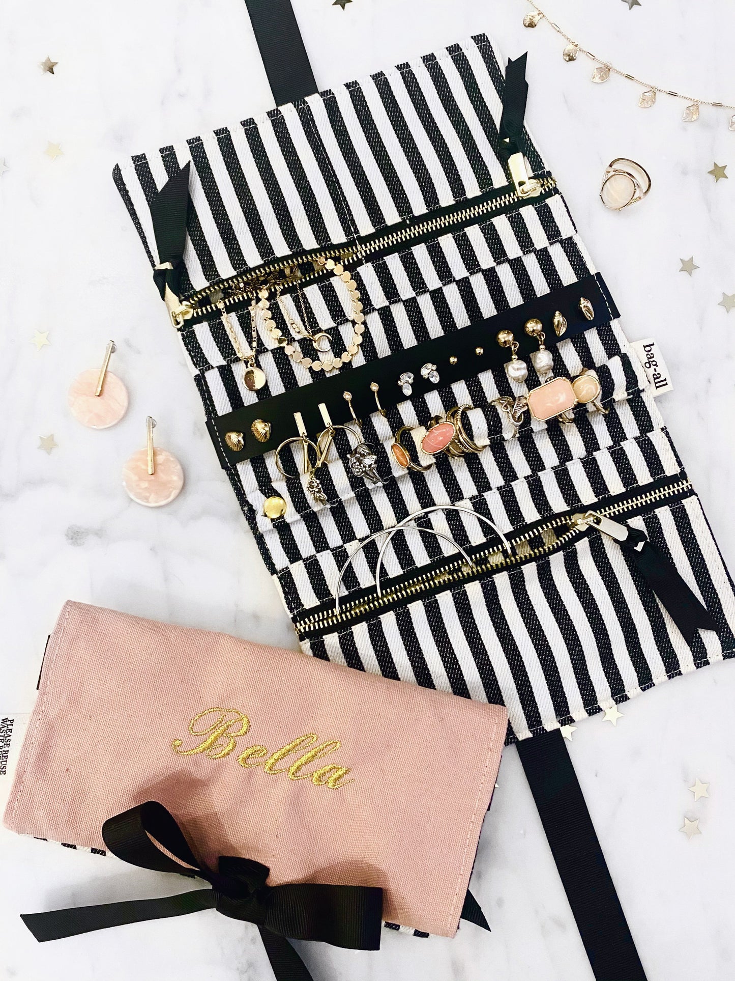Bag-all Jewelry Organizer Travel Pouch in pink with black and white striped interior, featuring multiple compartments, leather earring holder, and ring storage, shown unfolded with jewelry display