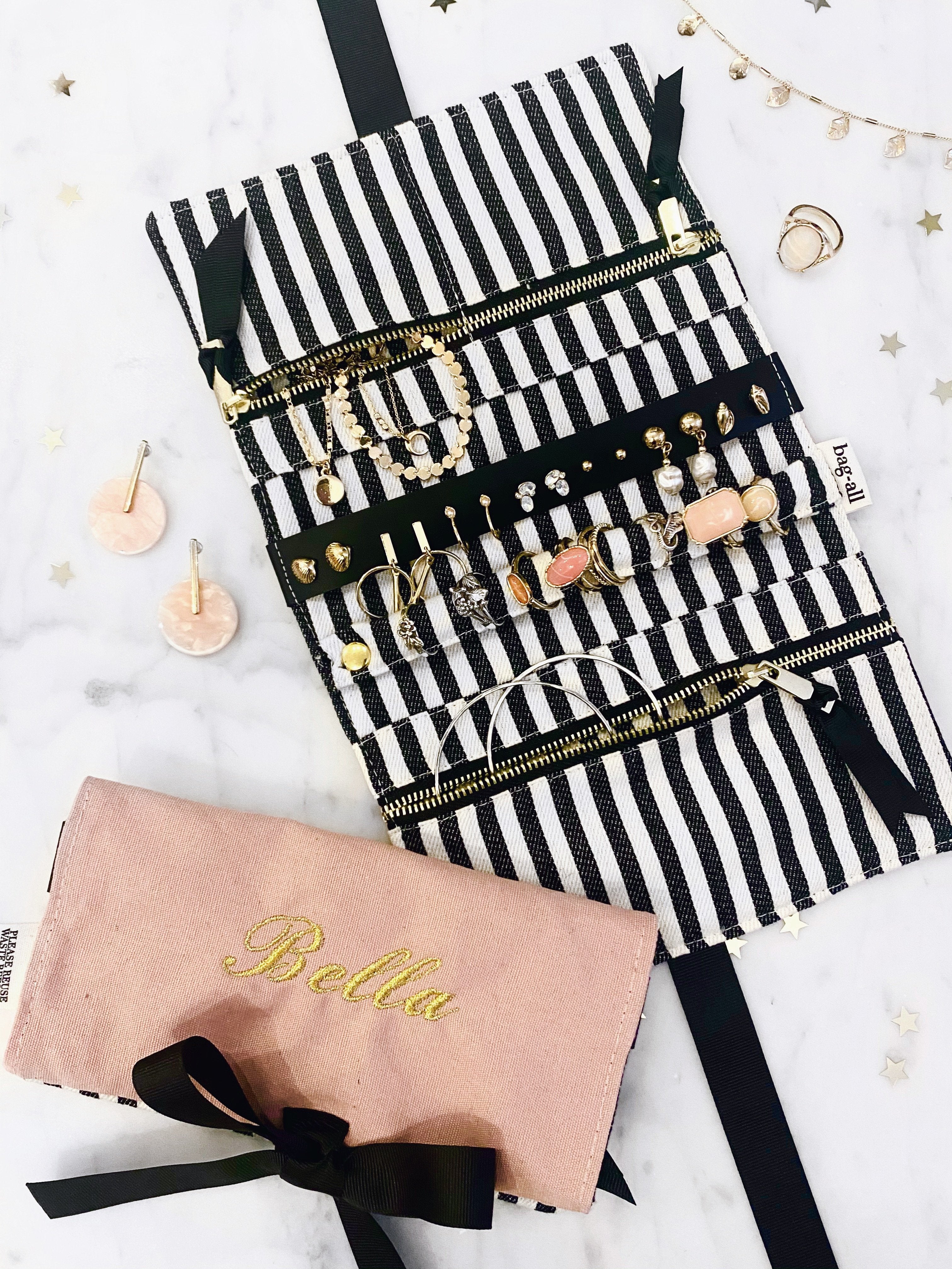 Bag-all Jewelry Organizer Travel Pouch in pink with black and white striped interior, featuring multiple compartments, leather earring holder, and ring storage, shown unfolded with jewelry display