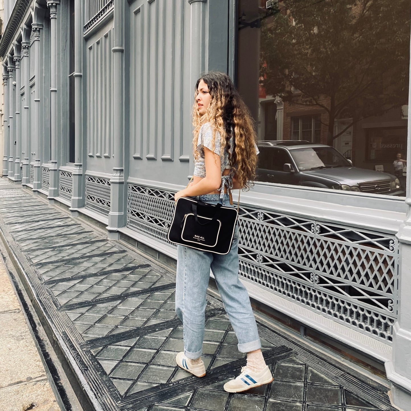 Bag-all black laptop case 13" with charger pocket worn by person on city street, showcasing practical design and urban style