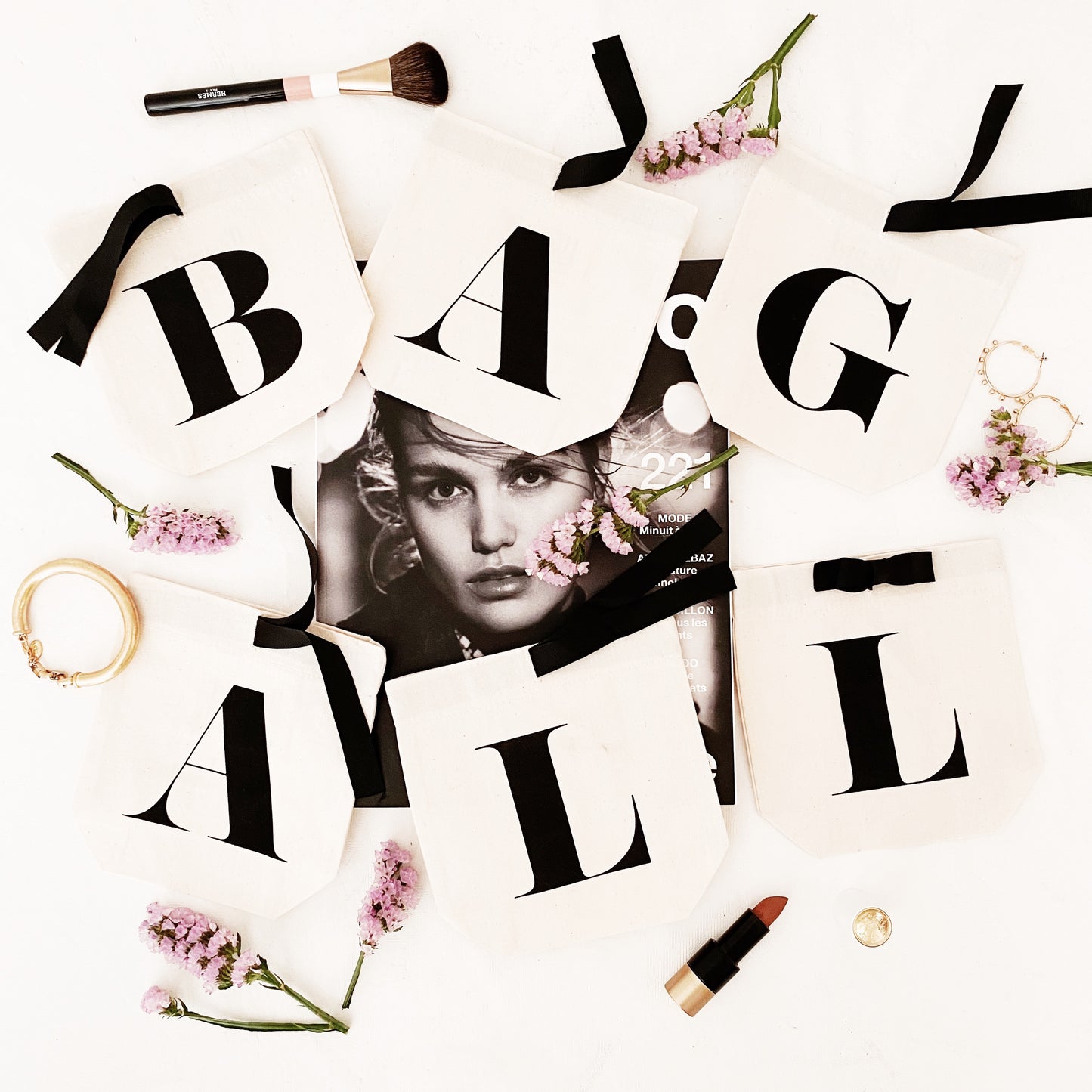 Bag-all Small Letter Bags Classic in cream with stylized typography, arranged with pink flowers, makeup brushes and lipstick on white background, perfect for organizing essentials