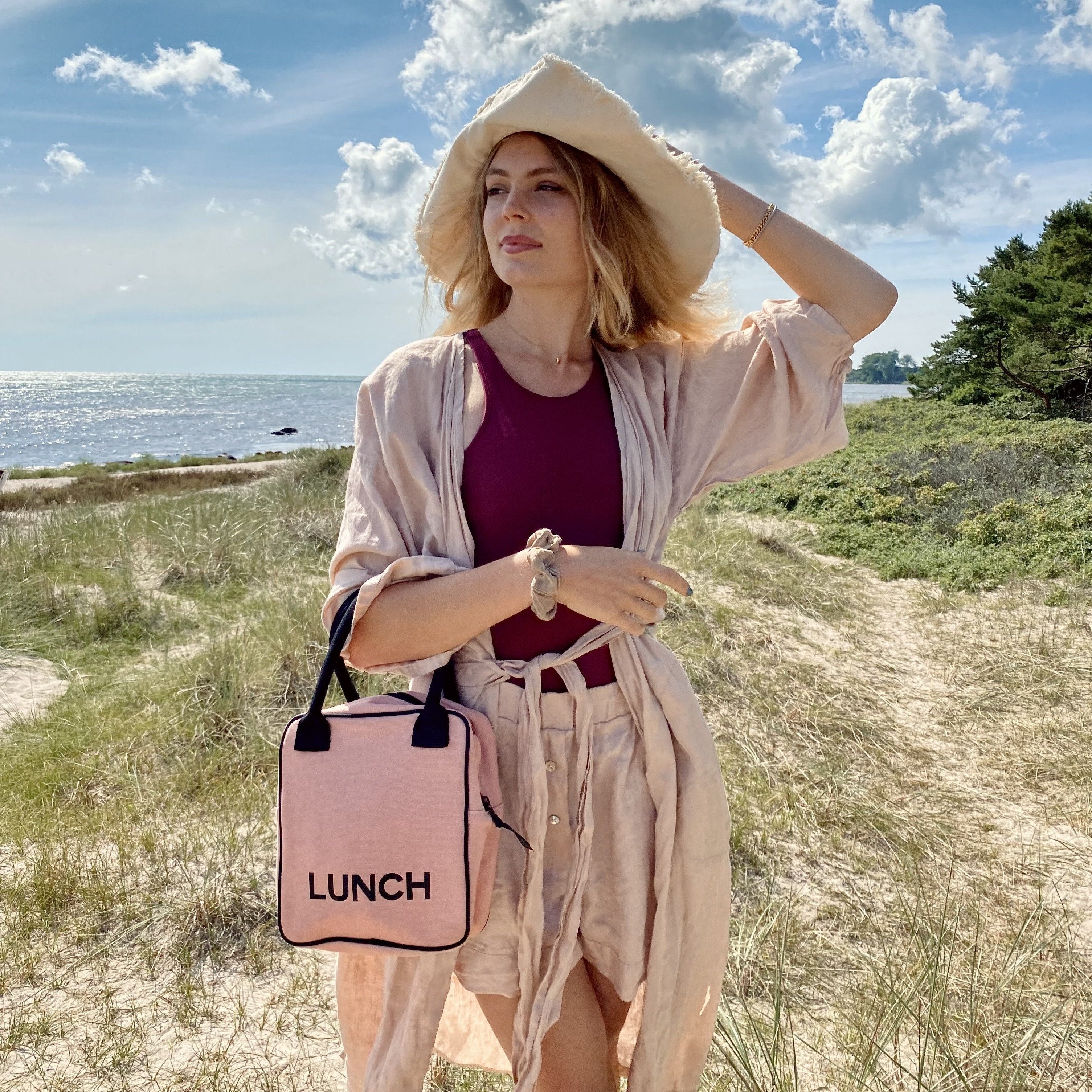 Bag-all Pink Lunch Box Insulated shown at beach, stylish blush-colored insulated lunch bag with black trim and LUNCH text, perfect for carrying meals outdoors
