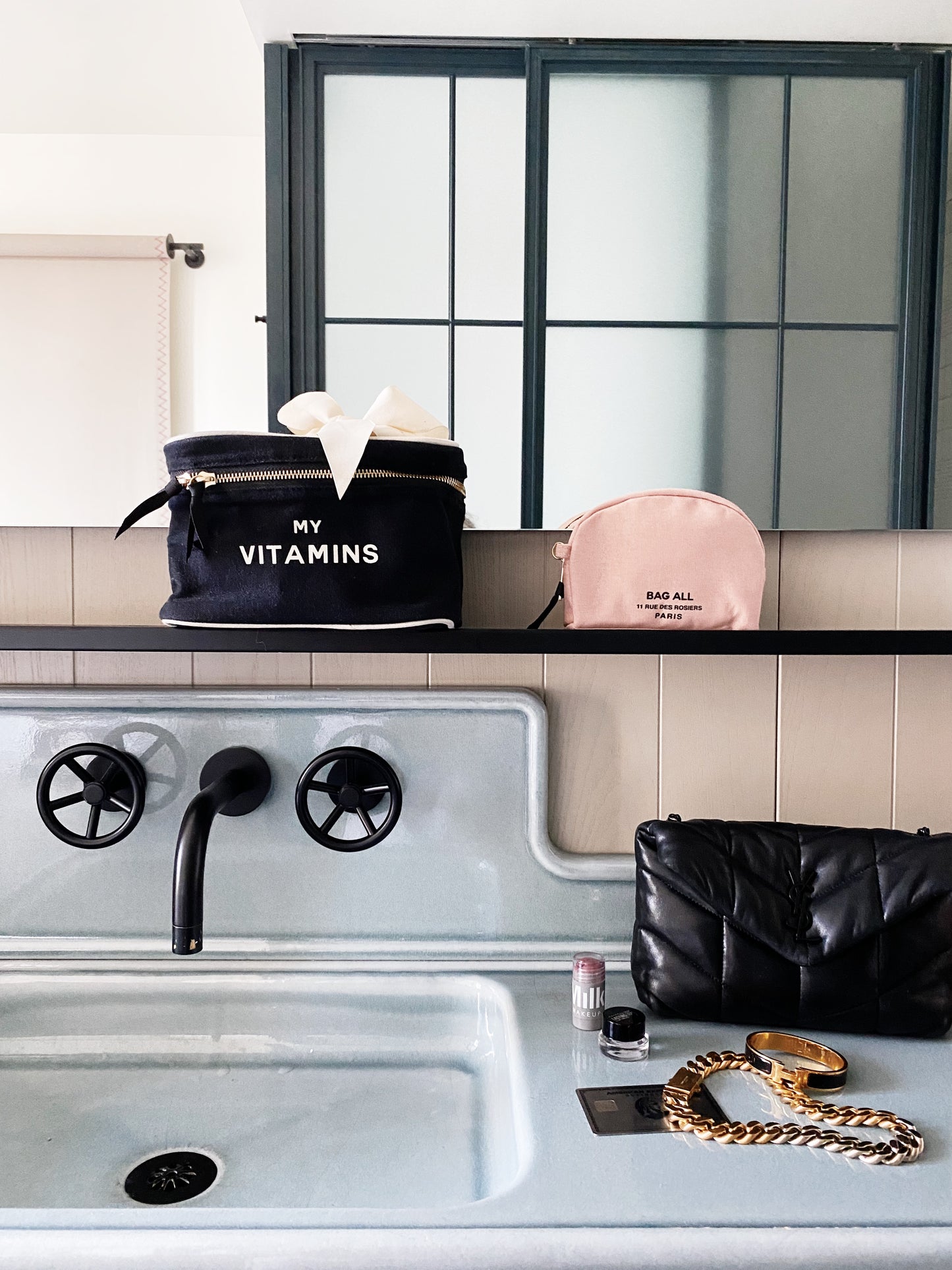Bag-all Vitamins Storage and Travel Box in black, displayed on bathroom counter alongside pink cosmetic case, showcasing stylish organization for daily supplements