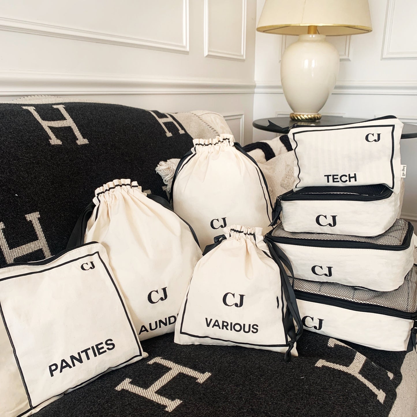 Bag-all personalized organizing bags and pouches for laundry, panties, tech items, and various accessories, shown with monogram CJ, displayed on H-pattern blanket